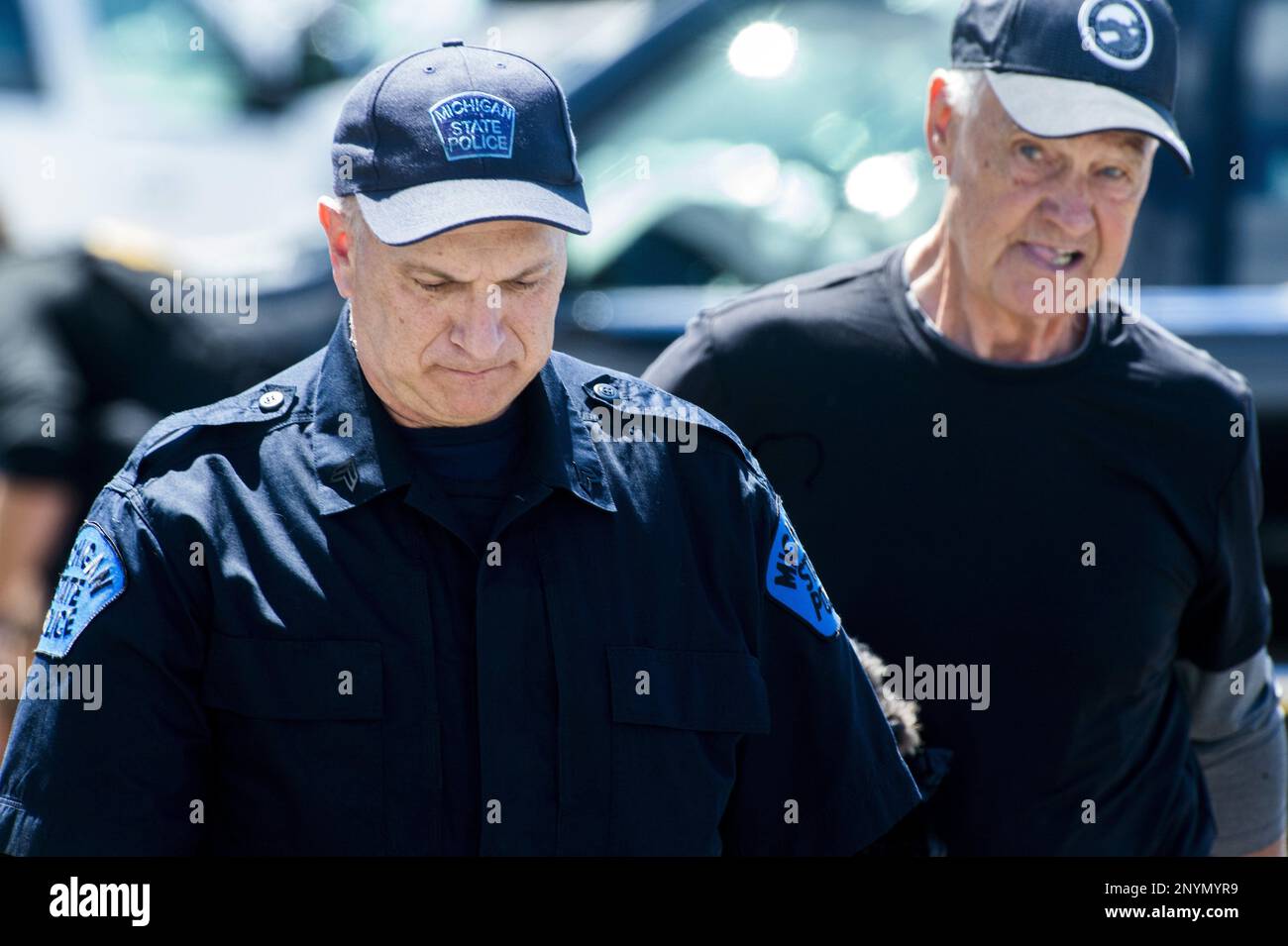 A Michigan State Police officer escorts a man at Bishop International Airport, Wednesday morning, June 21, 2017, in Flint, Mich. Officials evacuated the airport Wednesday, where a witness said he saw an officer bleeding from his neck and a knife nearby on the ground. Authorities say the injured officer's condition is improving. (Jake May/The Flint Journal-MLive.com via AP) Banque D'Images