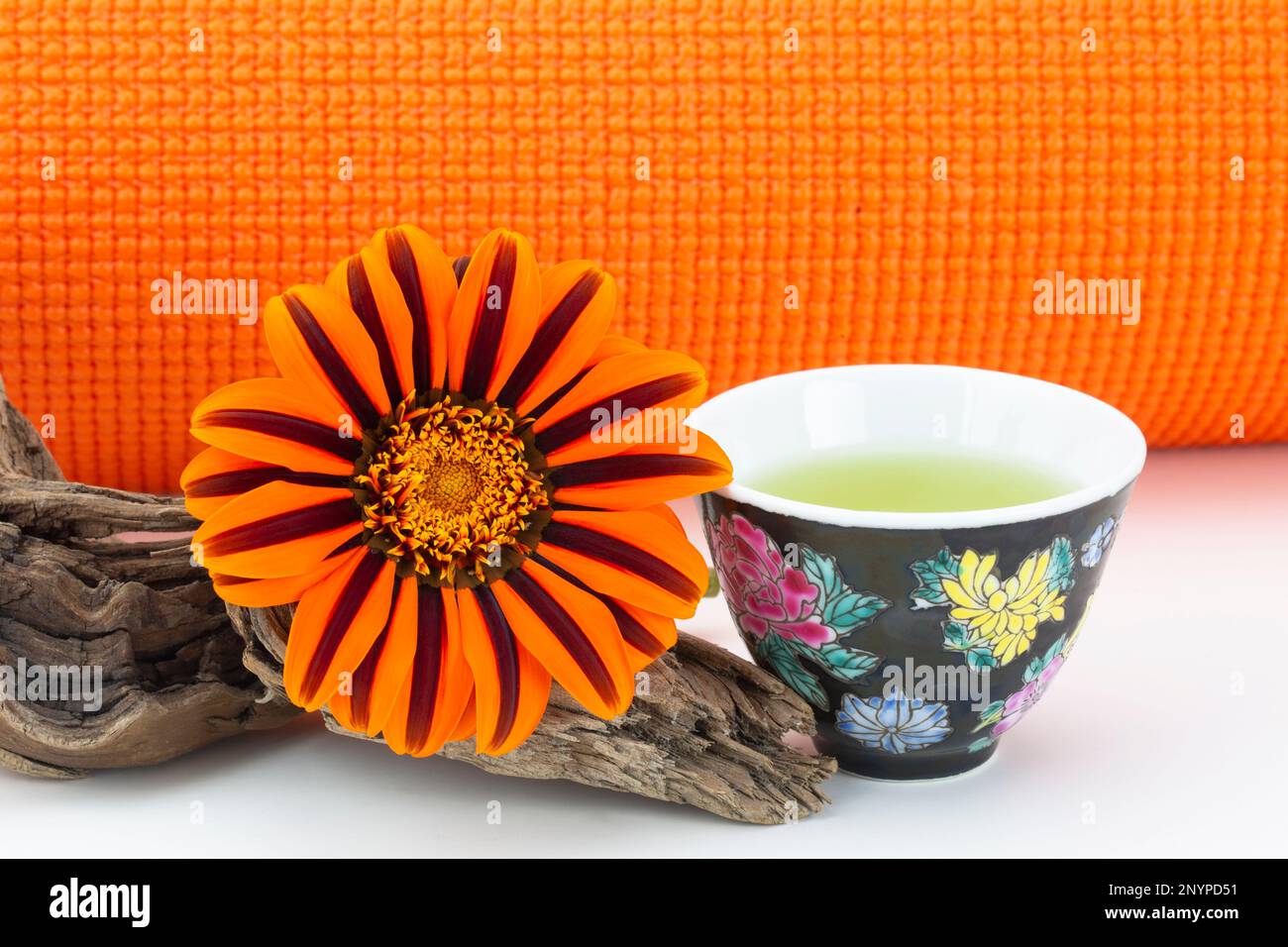 Exercice, hydratation et nature dans un équilibre sain vu dans le tapis de yoga orange, pétales orange naturels de fleur de Marguerite, et simple tasse de thé vert Banque D'Images