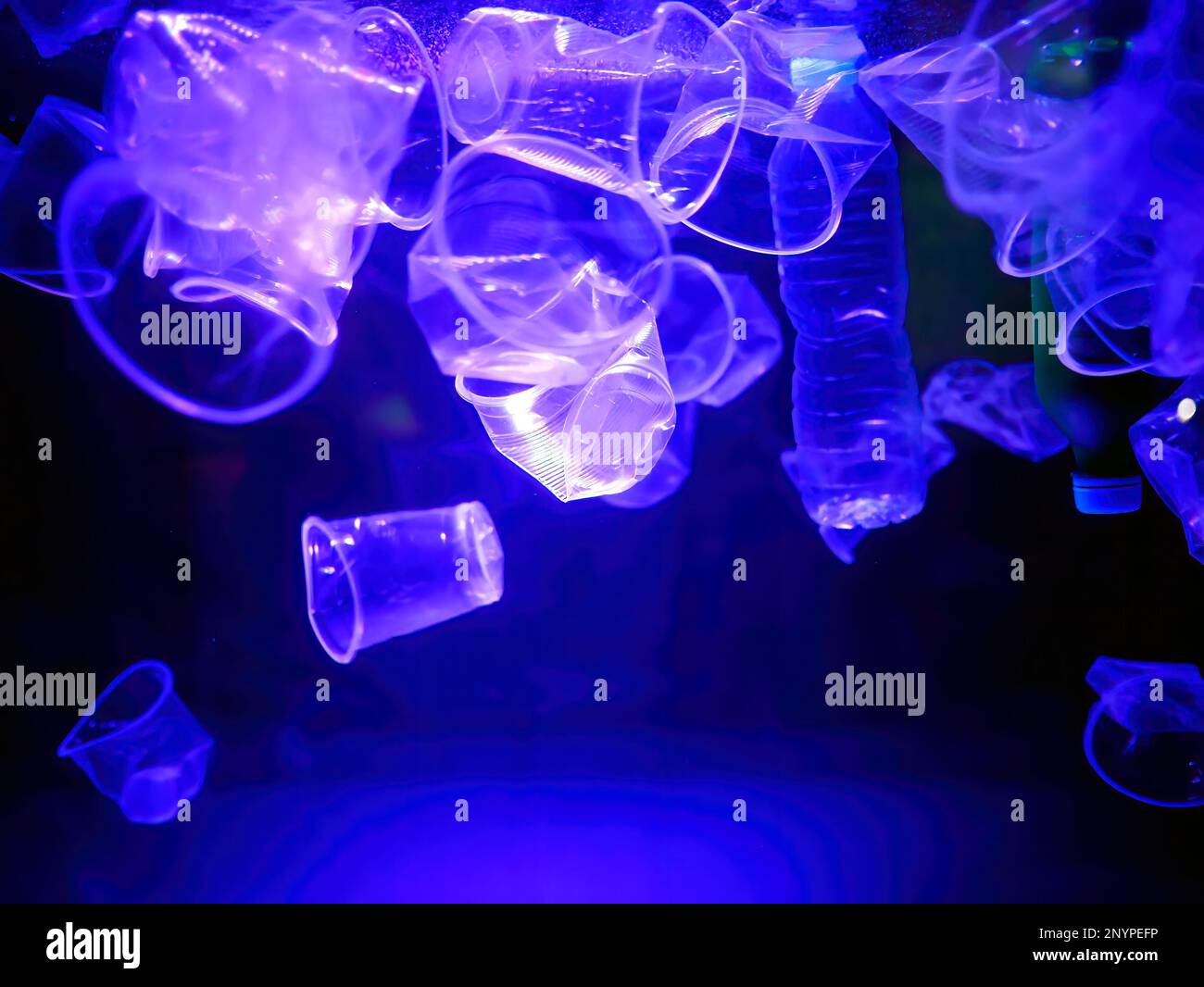 Tasses et bouteilles en plastique les déchets dérivent dans une lumière bleue illuminée eau, monochrome, pollution de l'environnement mondial, déchets sous-marins Banque D'Images