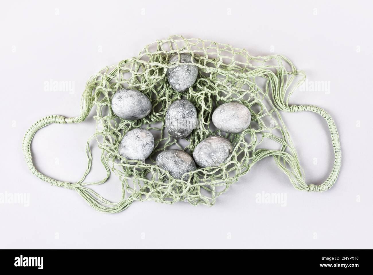 Œufs de Pâques gris dans un sac à ficelle vert sur fond gris. Minimalisme, espace de copie, pose à plat Banque D'Images