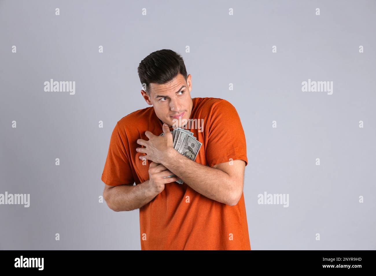 Homme cupide qui cache de l'argent sur fond gris Banque D'Images