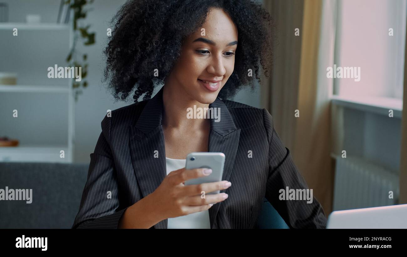 African american businesswoman freelance étudiante fille femme assis au bureau à domicile lire SMS email sur téléphone mobile travail en ligne par ordinateur développer Banque D'Images