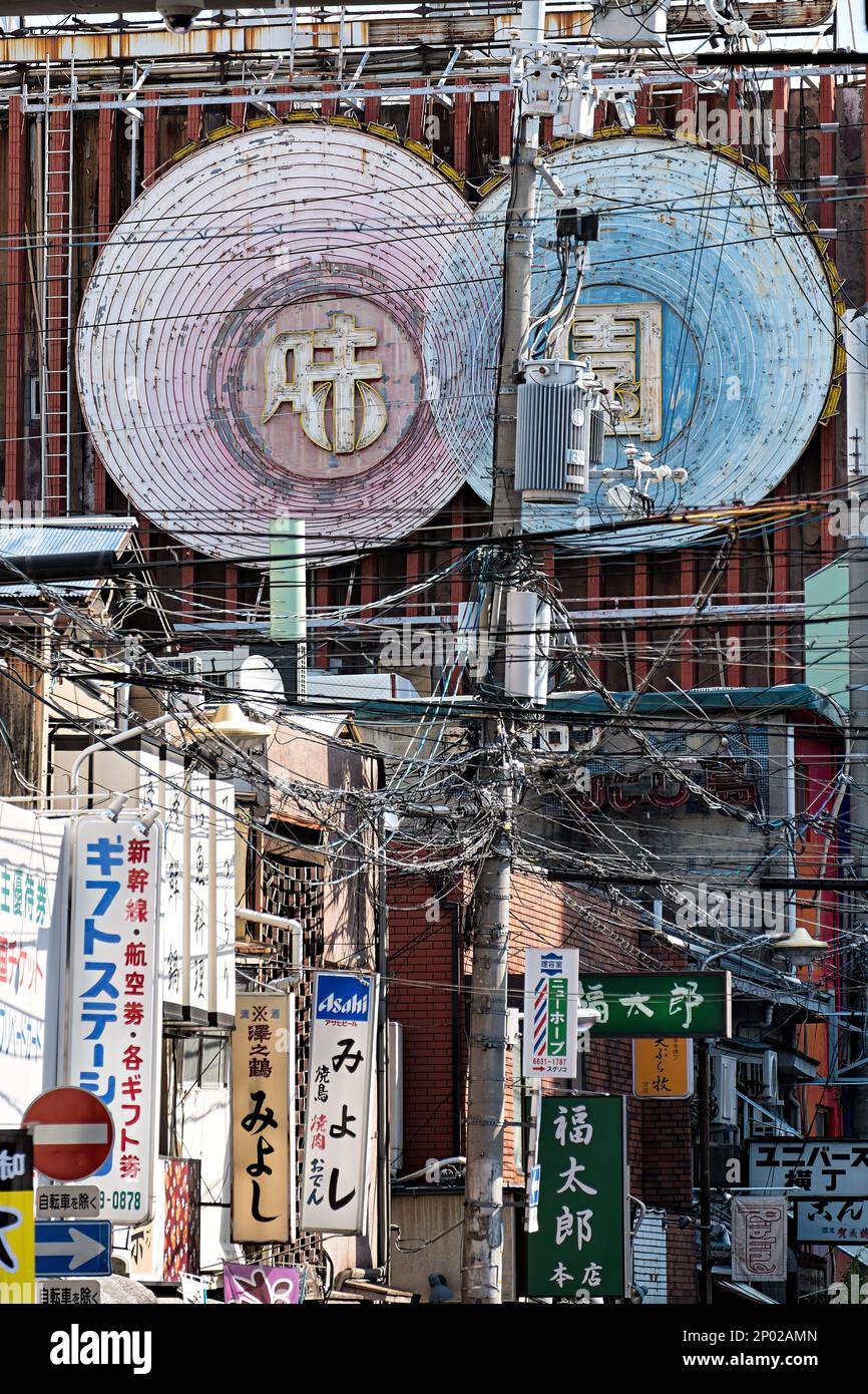 Des lignes électriques se sont emmêlées entre plusieurs panneaux publicitaires et panneaux dans une petite rue d'Osaka, au Japon Banque D'Images