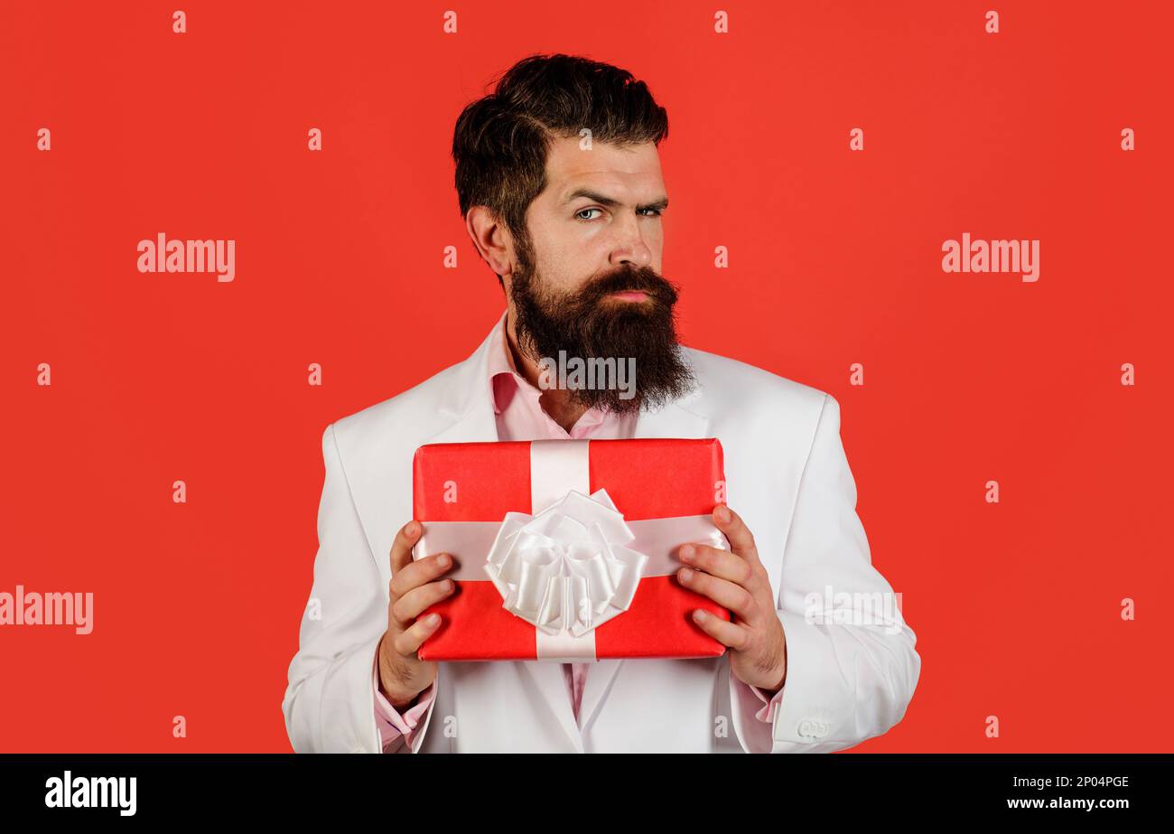 Beau homme avec boîte cadeau. Homme barbu sérieux en costume avec boîte cadeau. Un gars attrayant avec cadeau. Saint-Valentin, Fête des femmes ou des mères Banque D'Images