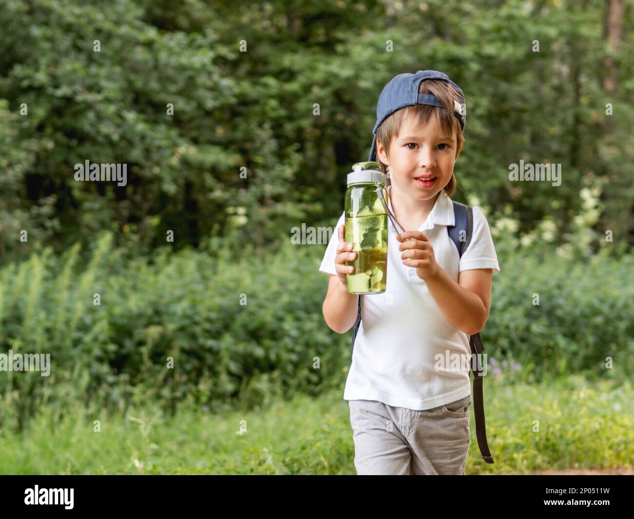 Un garçon assoiffé tient dans les mains un flacon vert réutilisable avec de l'eau pure. Activités de plein air en été. Un mode de vie sain. Banque D'Images