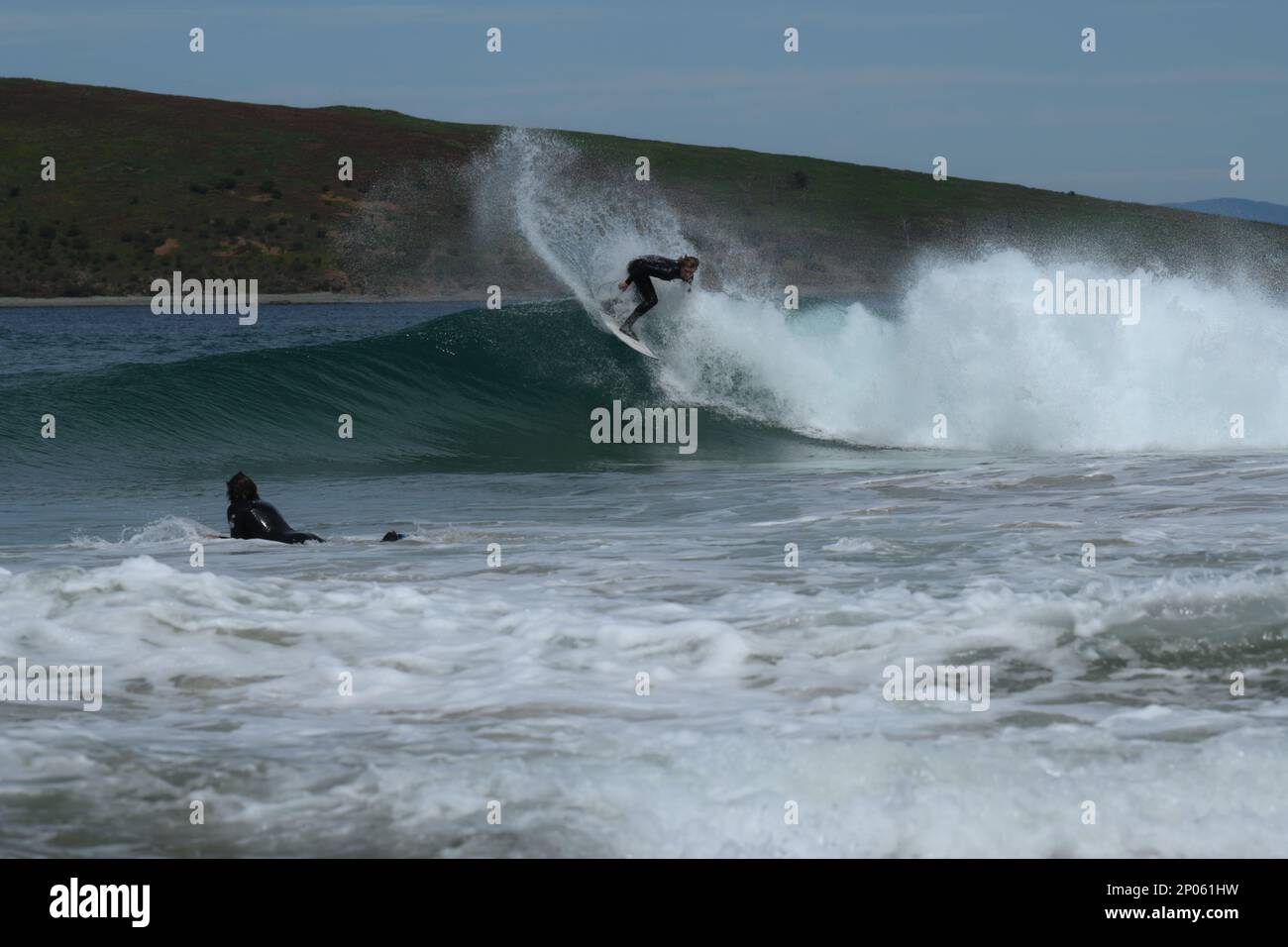 Un surfeur atteint le sommet de la vague envoyant un jet dans l'air devant le surfeur pagayant sur .Goes Island en arrière-plan Banque D'Images