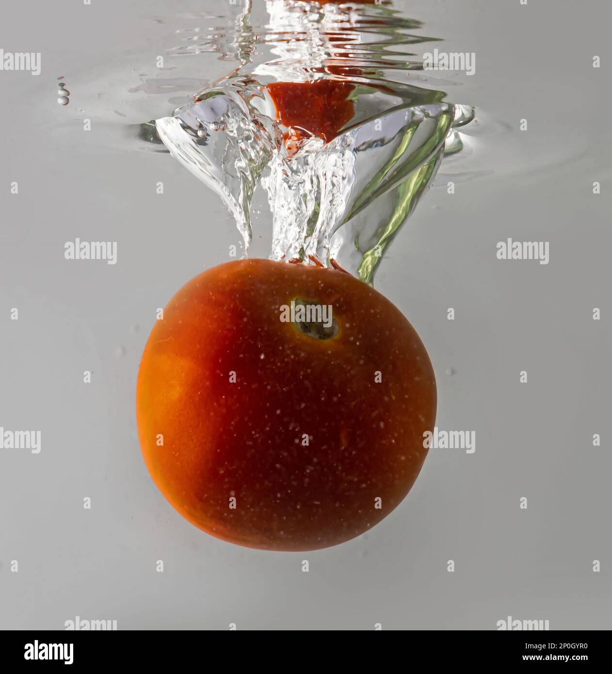 Tomate mûre tombe profondément sous l'eau avec un grand bruit. Banque D'Images
