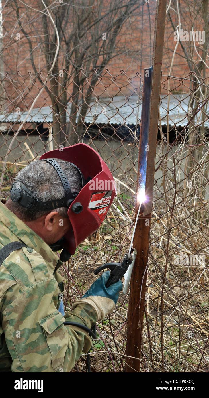 Un soudeur dans une veste de camouflage et un masque de protection rouge  avec l'inscription en russe « masque de soudage F5 » travaille avec une  machine à souder Photo Stock - Alamy