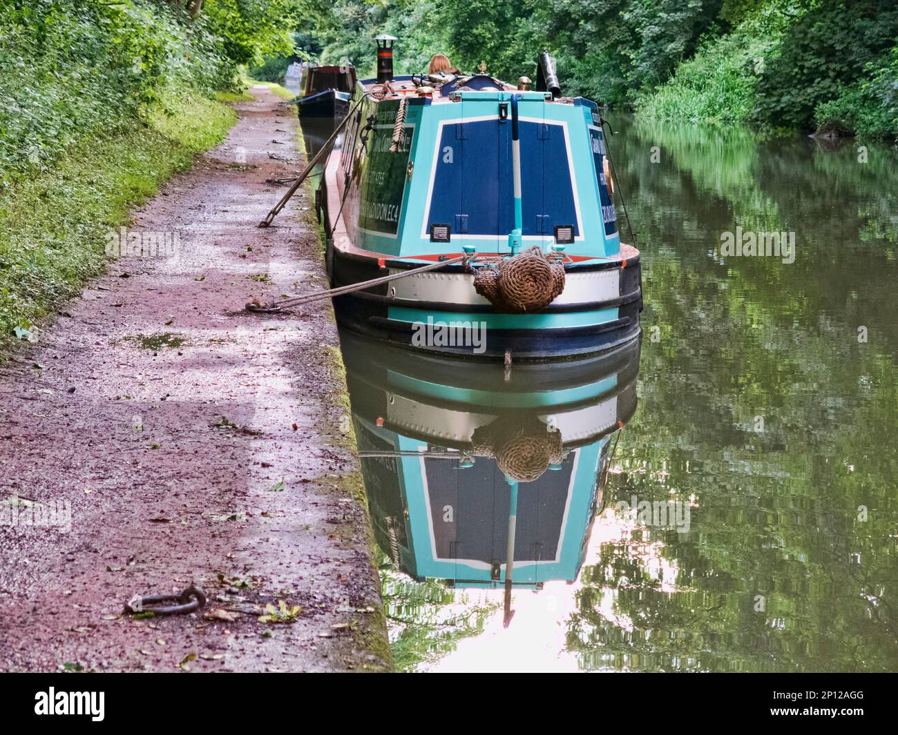 Un ancien bateau narrowboat historique coloré amarré le long du chemin de halage sur un canal en Angleterre, reflété dans l'eau Banque D'Images