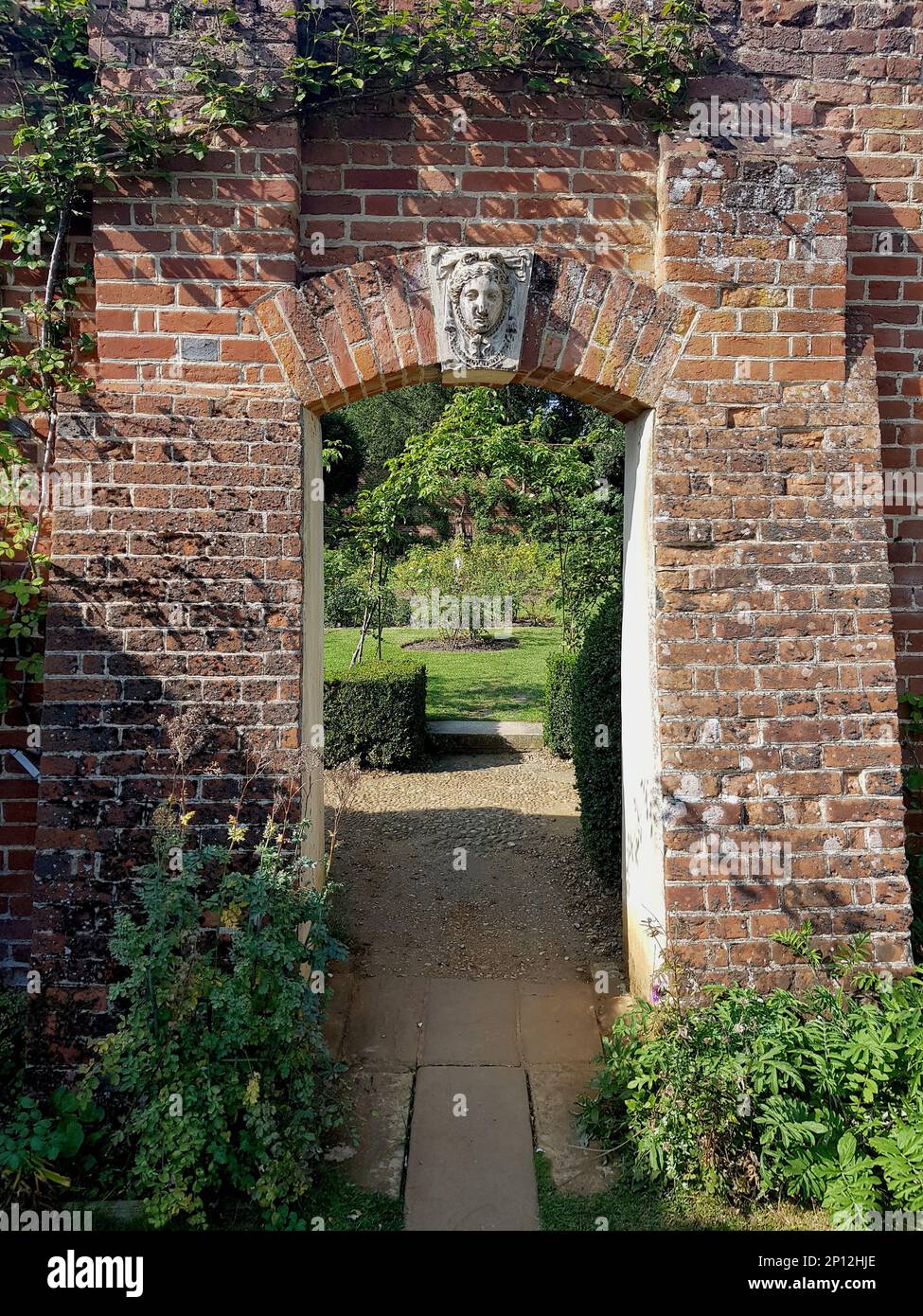 Vue sur une entrée de jardin par un vieux mur de briques. Banque D'Images