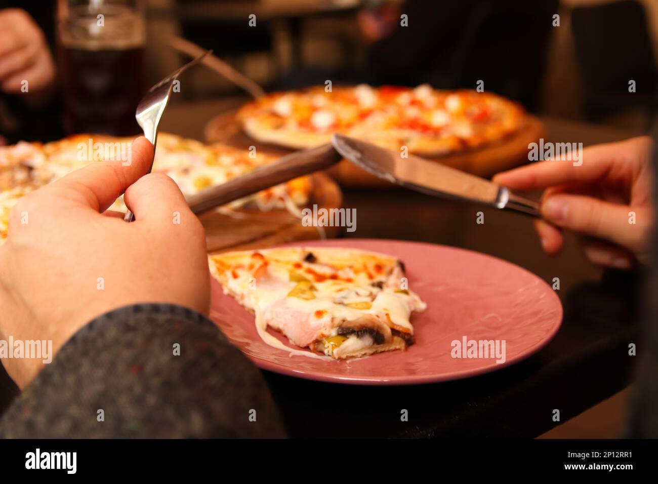Pizza avec couteau et fourchette. Main mâle. La personne de Defocus coupe la pizza dans le café. Jeune homme affamé avec couteau et fourchette de couper et de manger de la pizza dans le café Banque D'Images