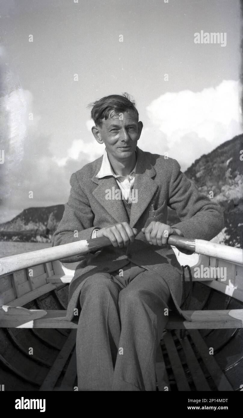 Années 1950, historique, homme dans une veste en laine et un pantalon utilisant des rames comme il rame un petit bateau en bois, Angleterre, Royaume-Uni. Banque D'Images