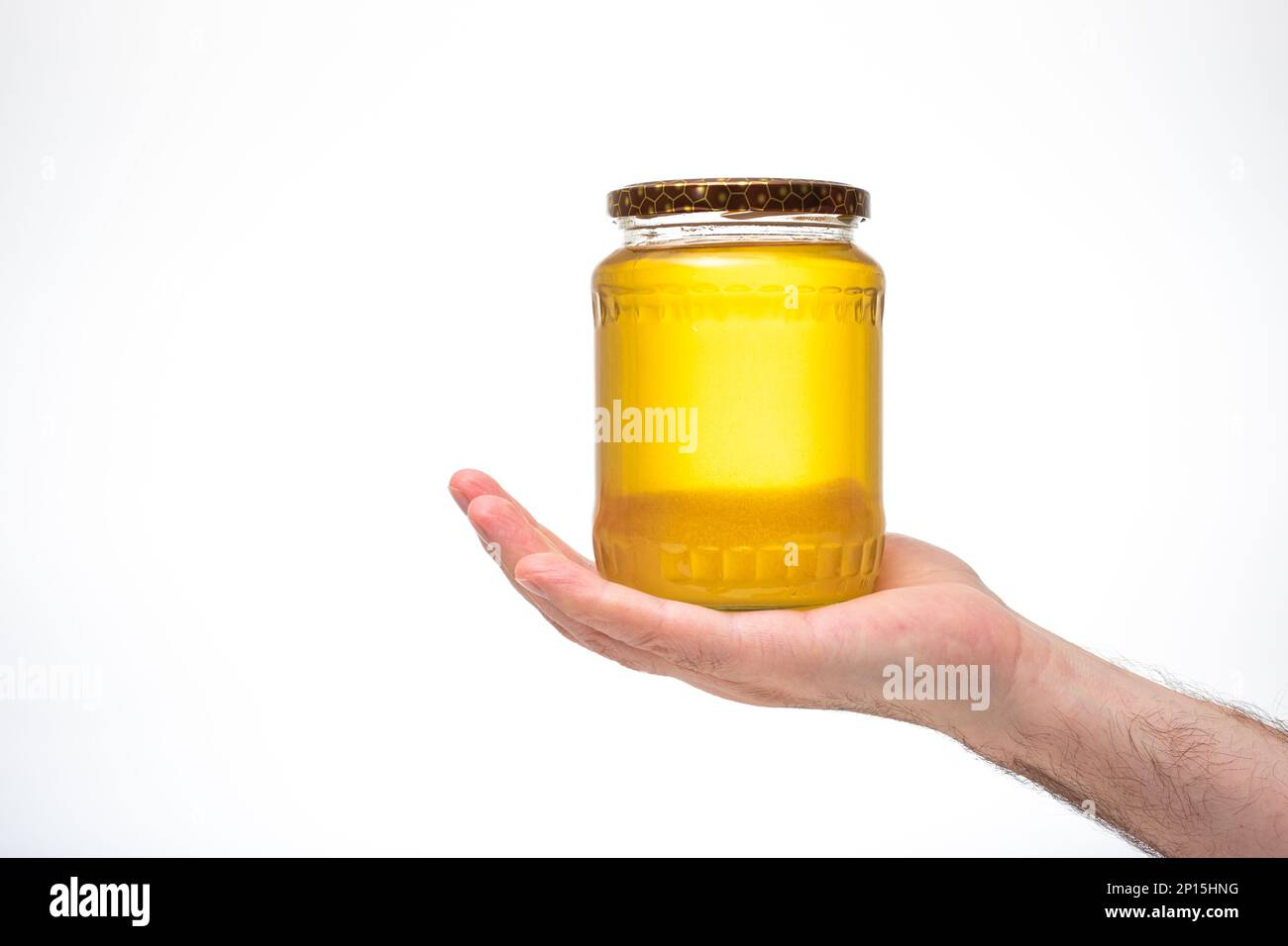 Miel d'abeille jaune d'or frais dans un pot en verre, tenu par la main mâle caucasienne. Gros plan en studio, isolé sur fond blanc. Banque D'Images