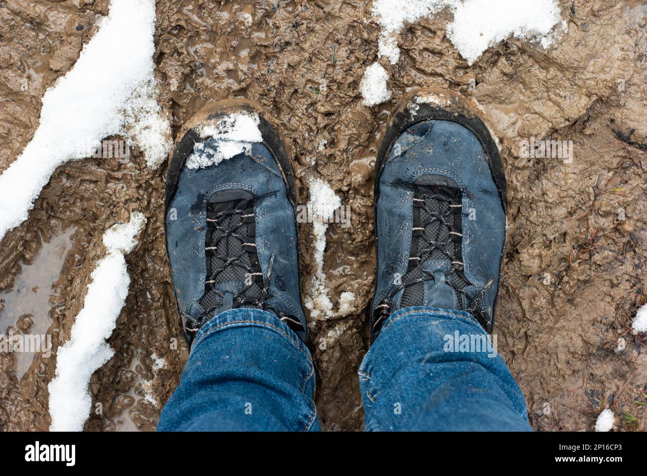 Bottes sales résistantes aux intempéries dans une flaque de boue de forêt avec un Jean bleu neige en fusion vue du dessus. Banque D'Images