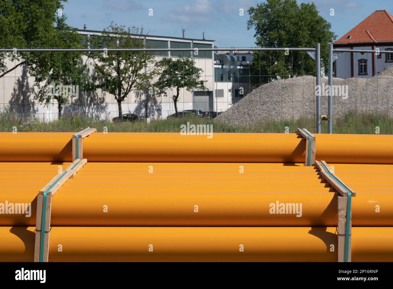 Tuyaux en plastique orange le long d'une clôture en treillis métallique. Chantier de construction en arrière-plan. Banque D'Images