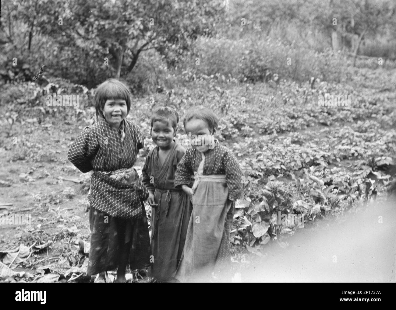 Trois enfants Ainu debout dans un jardin, 1908. Banque D'Images