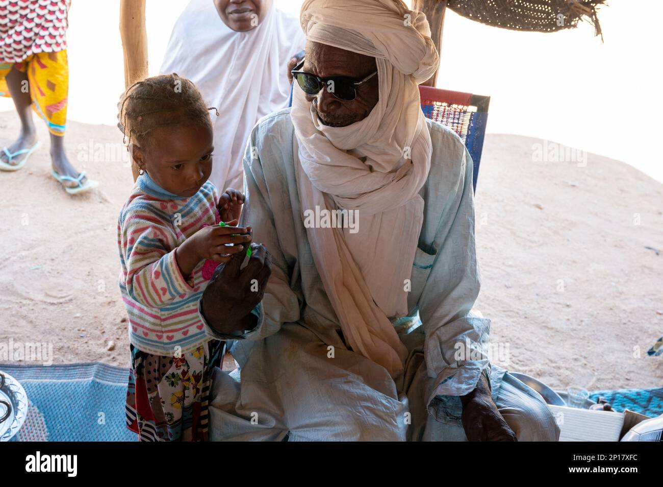 Un chef de village donne à une fille une bouteille de « bulles » dans un village près d'Agadez, au Niger, le 04 janvier 2023. Les dons ont été fournis par des groupes privés et par Ramstein Middle School, en Allemagne, qui voulaient fournir des articles à des ressortissants locaux dans une zone relevant de la responsabilité de l’escadre expéditionnaire de 435th. Le bataillon des affaires civiles de 443 a facilité le transfert des dons au FAN ACM, à distribuer aux villages locaux, aux organisations de femmes et aux orphelinats d’Agadez et des environs. Banque D'Images