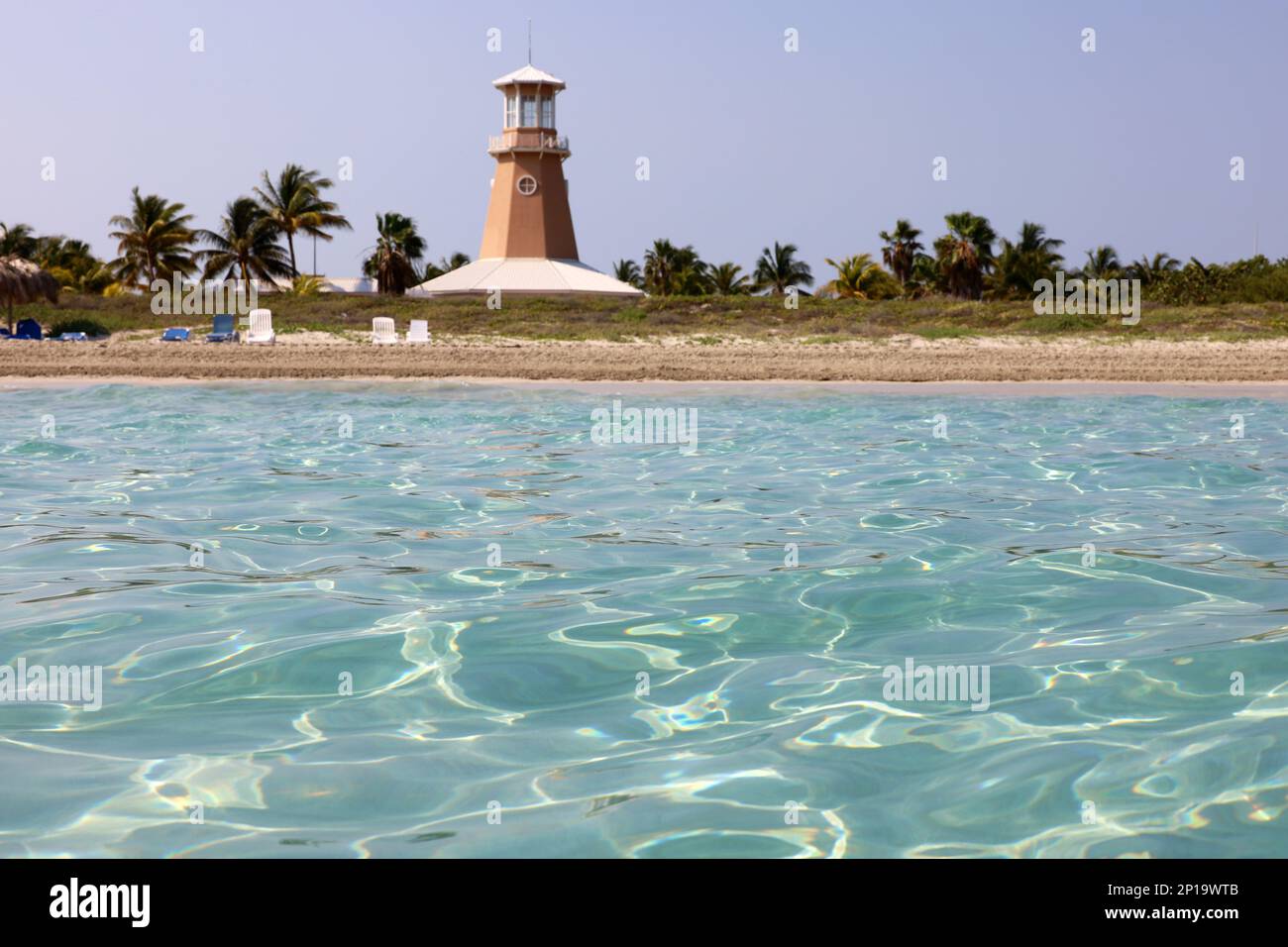 Vue imprenable de la surface de l'eau à la plage tropicale avec phare, chaises longues et palmiers à noix de coco. Station balnéaire sur l'île des Caraïbes Banque D'Images