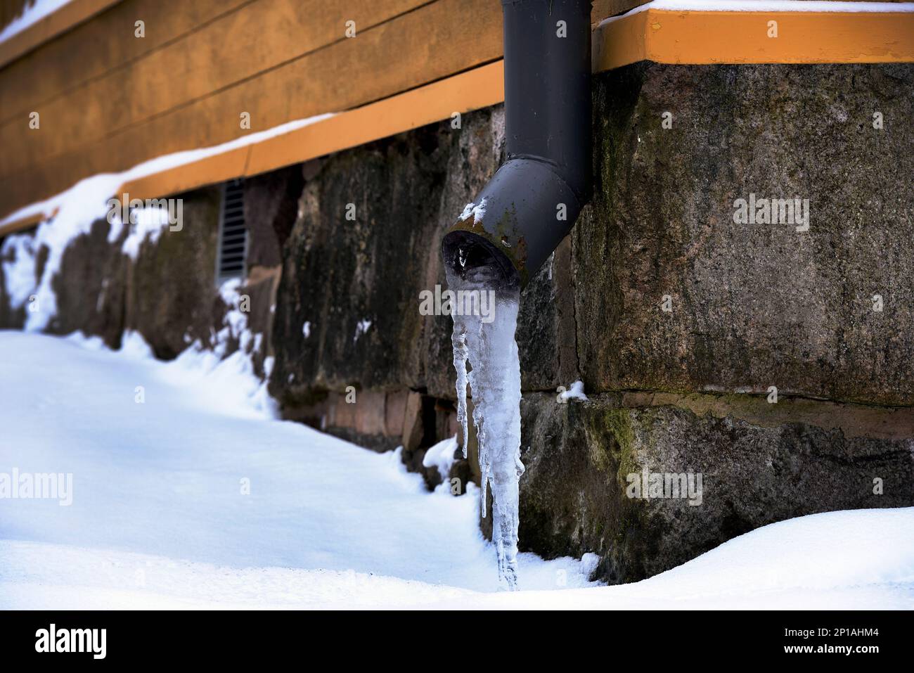 drainpipe de glace près de la fondation en pierre d'une vieille maison en hiver Banque D'Images