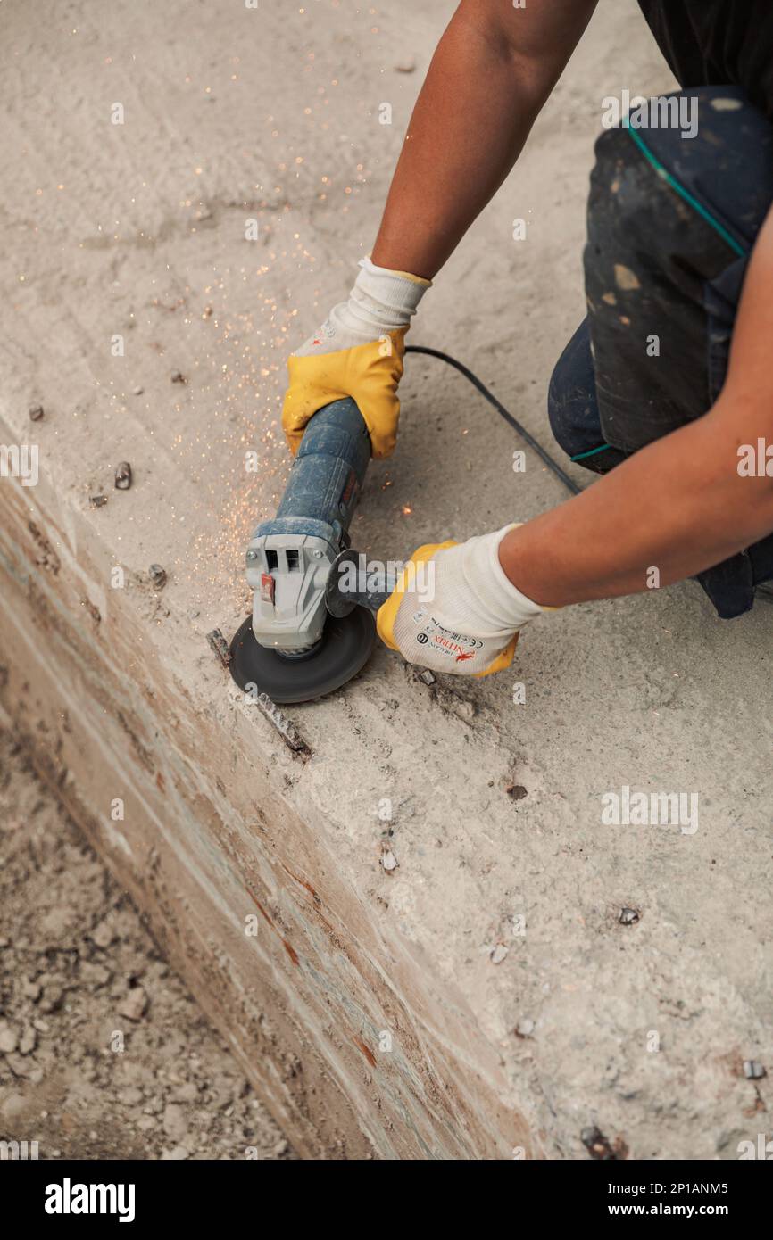 Mains d'un homme avec des gants utilisant une machine électrique de coupe en acier pendant le travail Banque D'Images