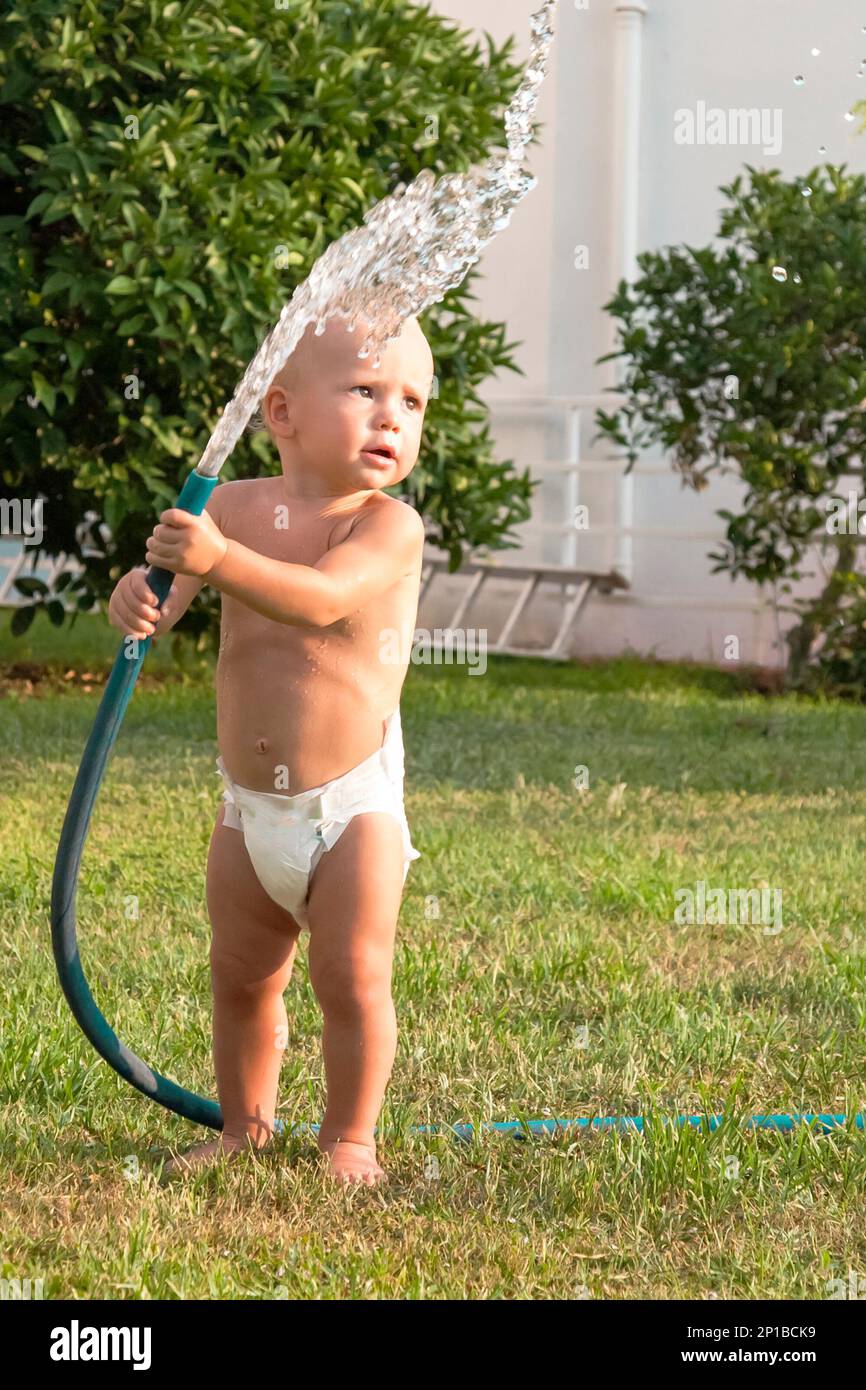 Enfant garçon jouant avec le tuyau d'eau à l'extérieur en été, enfance heureuse Banque D'Images