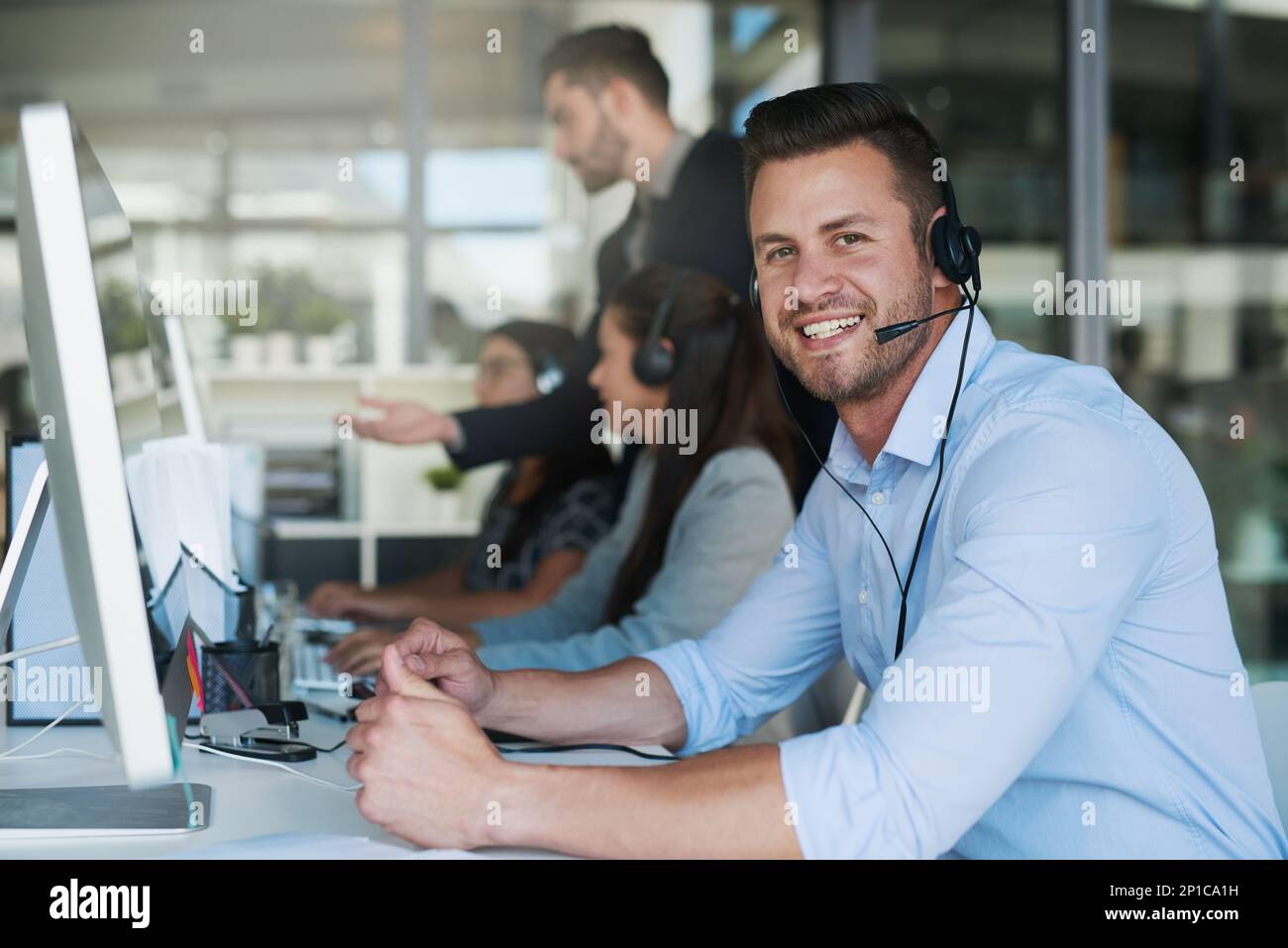 Le service est excellent pour les affaires. Portrait d'un jeune homme heureux et confiant travaillant dans un centre d'appels. Banque D'Images