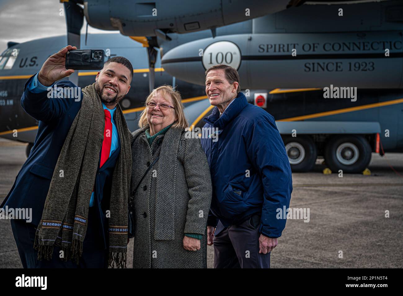 Les représentants de l'État du Connecticut Hubert D. Delany, Jane Garibay et le sénateur Richard Blumental posent pour un selfie devant l'avion C-130H Hercules peint de l'aile du pont aérien 103rd à la suite de la cérémonie de bienvenue du groupe d'entretien 103rd à la base de la Garde nationale aérienne Bradley, East Granby (Connecticut), le 4 février 2023. L'avion a été spécialement peint pour commémorer le 100th anniversaire de l'aile du transport aérien de 103rd. Banque D'Images