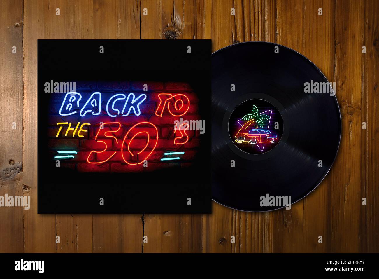 Gros plan sur panneau de bois avec un disque de vinyle sur son milieu avec une fausse compilation de chansons du 50s sur un bureau en bois. Banque D'Images