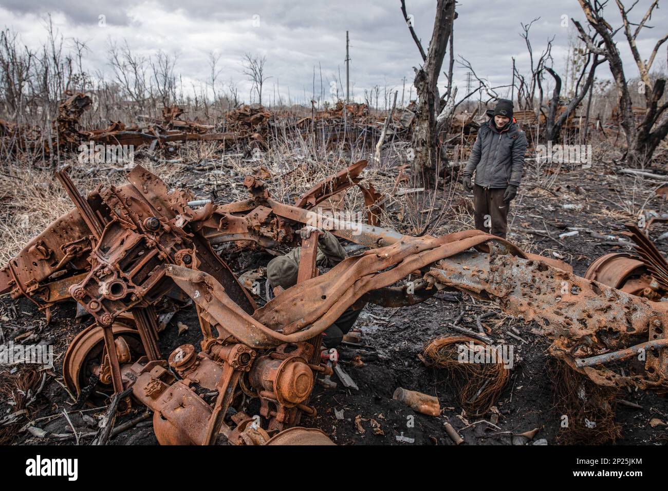 Des hommes locaux démantelent les restes de matériel militaire russe détruit et brûlé pour la ferraille, région de Kharkiv, Ukraine. En longeant les routes de la région de Kharkiv, plus vous vous rapprochez du Donbass, plus vous voyez de matériel militaire brûlé et cassé sur le bord de la route, dans les champs et les ceintures forestières. Dans l'une de ces ceintures forestières, nous avons vu une énorme quantité d'équipement russe brûlé. Quand nous nous sommes arrêtés pour prendre des photos, nous avons vu plusieurs hommes et adolescents systématiquement le faire passer. Ils le démontaient pour la ferraille, pour laquelle ils reçoivent 2 hryvnias par kilogramme. Ils ne peuvent pas collecter plus t Banque D'Images