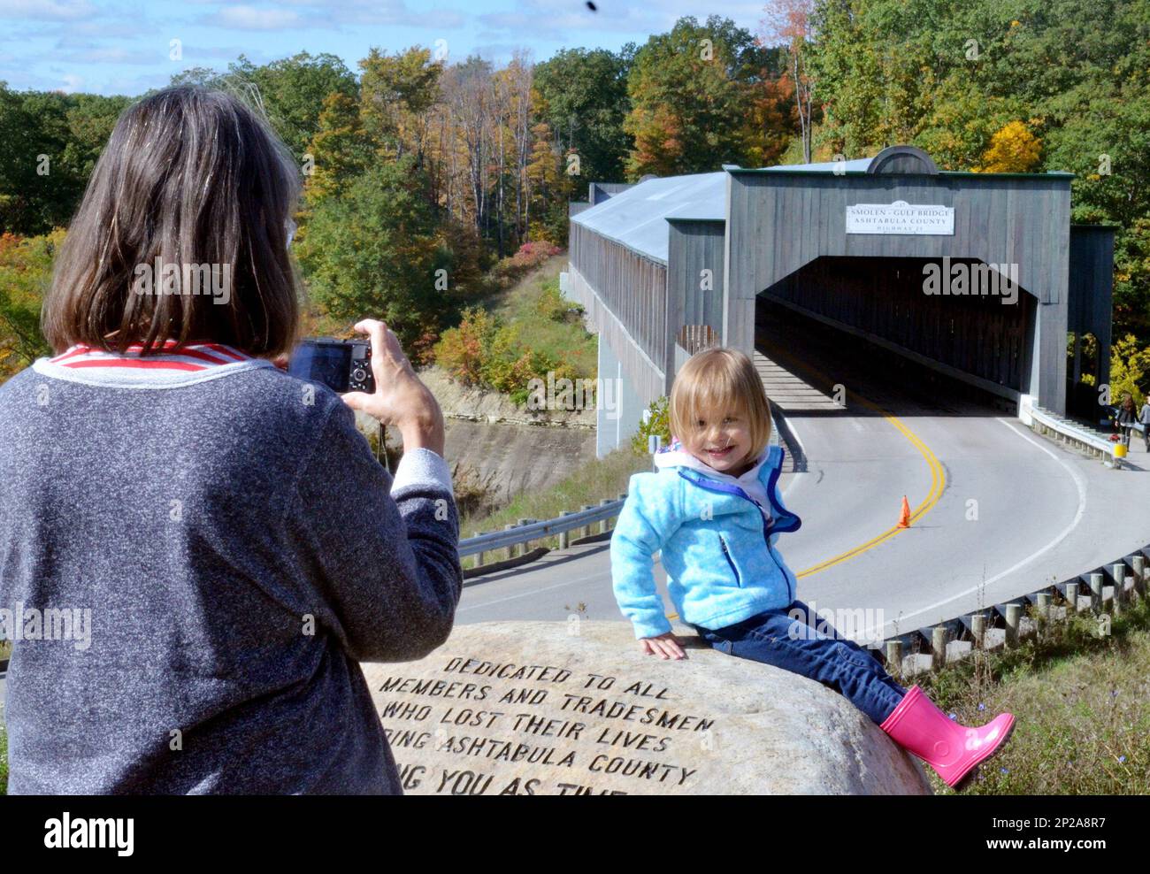 Trudy Mueller, left, of Conneaut, Ohio takes a picture of her granddaughter, Eden Williams, 2, of Jefferson, Ohio at the Gulf Smolen Bridge in Plymouth Township, Ohio during the Ashtabula County Covered Bridge Festival on Saturday, Oct. 10, 2015. The festival spans 18 covered bridge sites in the area. (Warren Dillaway/Ashtabula Star Beacon via AP) Banque D'Images