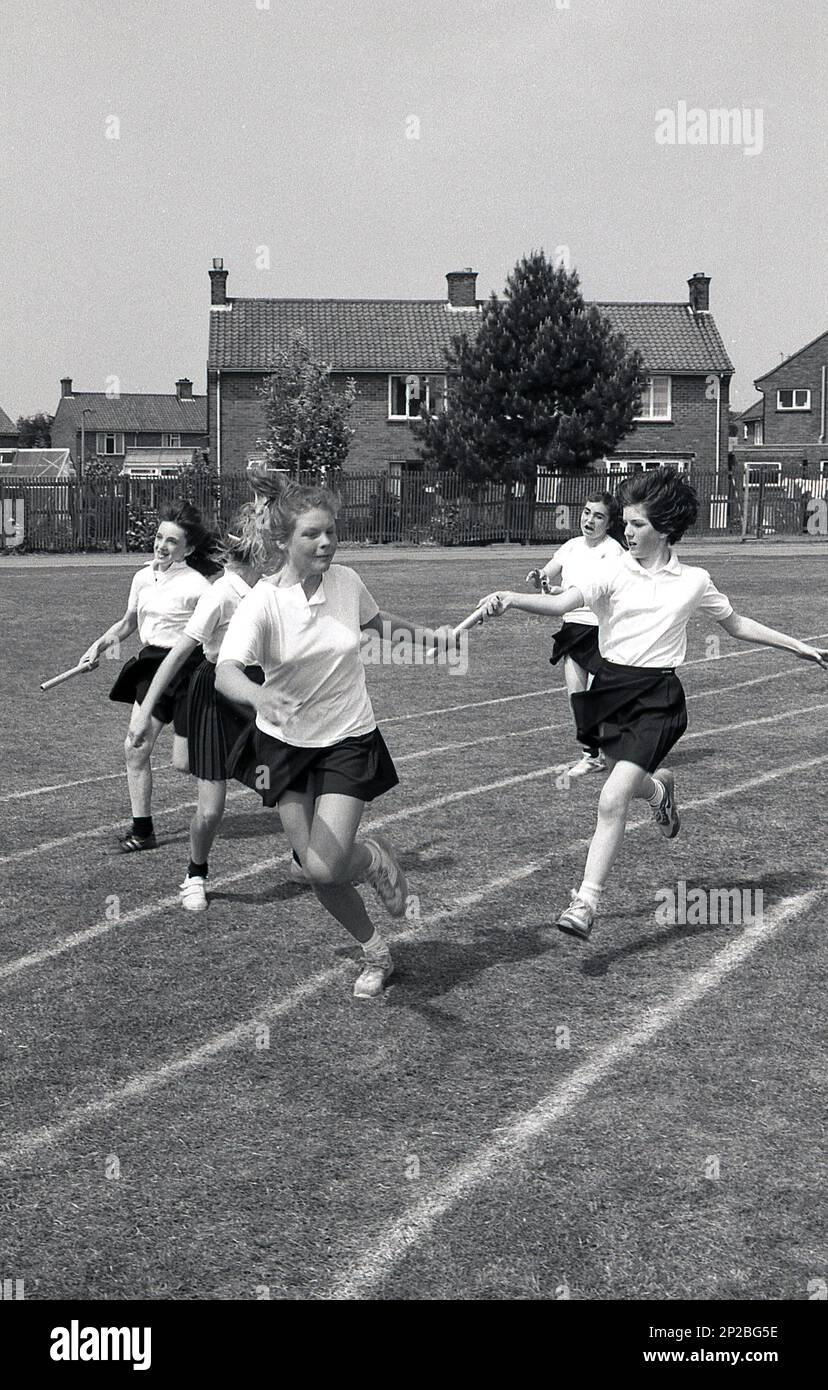 1989, journée des sports de l'école secondaire, à l'extérieur sur un terrain de sport, de jeunes adolescentes qui s'affrontent dans une course de relais, remettant le bâton à leurs coéquipiers, Angleterre, Royaume-Uni. Banque D'Images