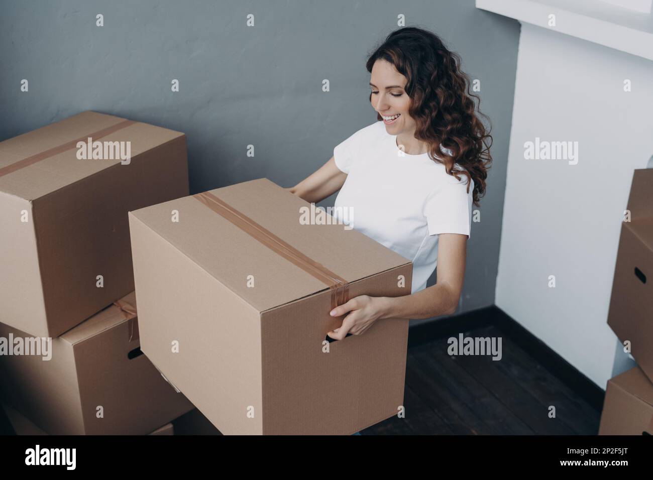 Femme hispanique souriante propriétaire d'une maison locataire tenant une boîte en carton avec des effets personnels, déménageant dans un nouvel appartement. Bonne fille apporte des choses Banque D'Images