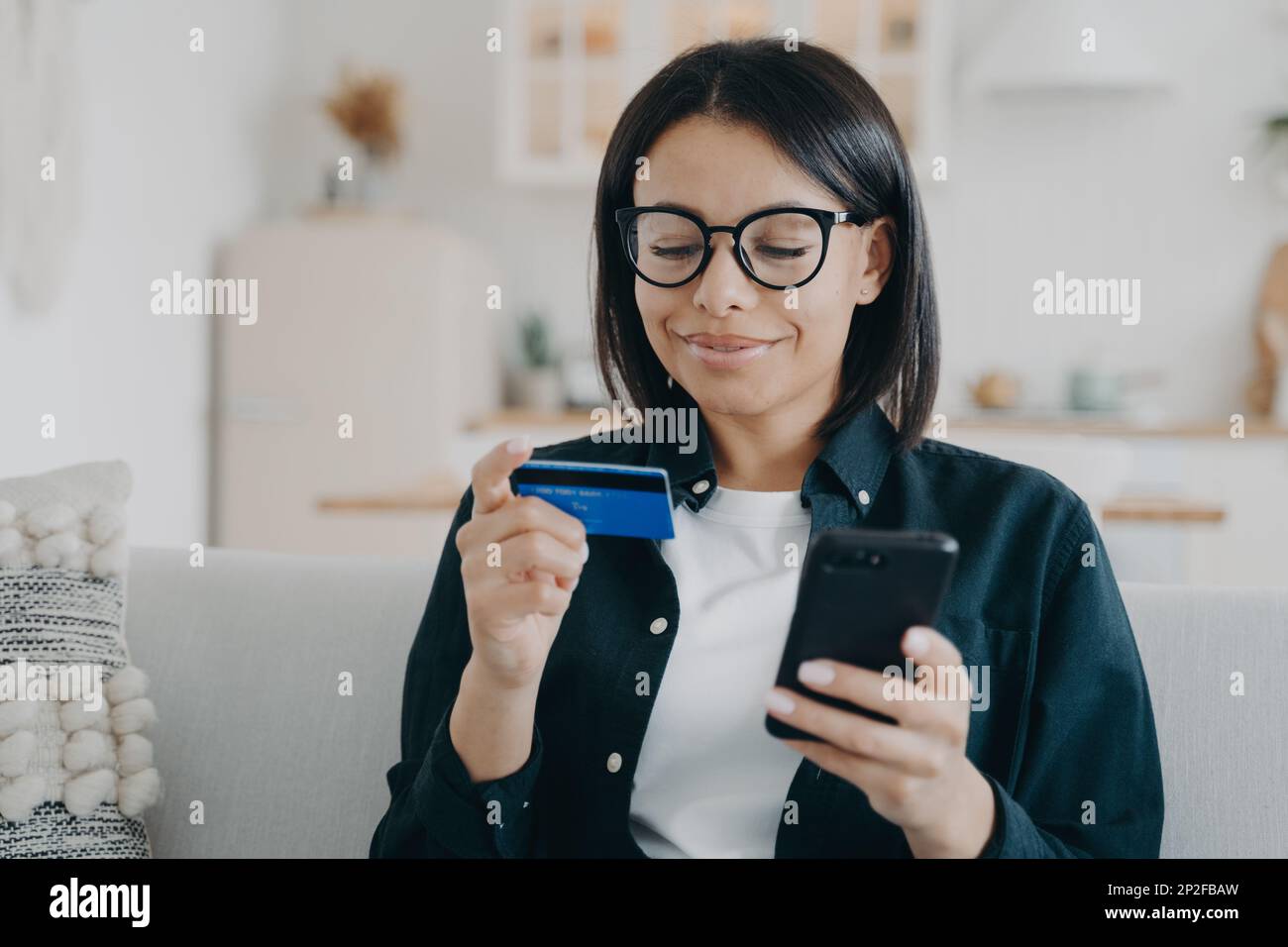 Une femme souriante dans des lunettes tenant une carte de crédit bancaire et un smartphone utilise le service bancaire en ligne à la maison. Bonne femme paie pour les achats, achats sur int Banque D'Images