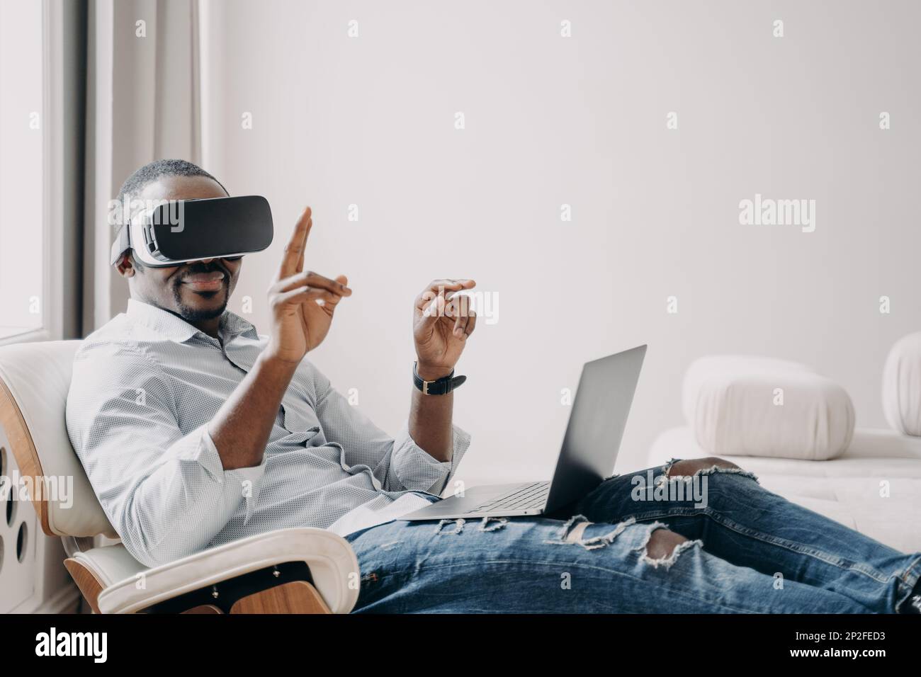 L'homme afro-américain en lunettes vr travaille chez lui. Un homme d'affaires décontracté clique sur des boutons virtuels. Travail à distance et jeux futuristes. Numérique moderne Banque D'Images