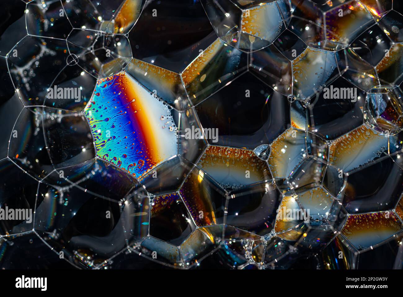 Gros plan, photo macro d'une bulle de savon, arc-en-ciel multicolore avec couleurs jaune, violet, rose, bleu et vert sur fond noir. Banque D'Images