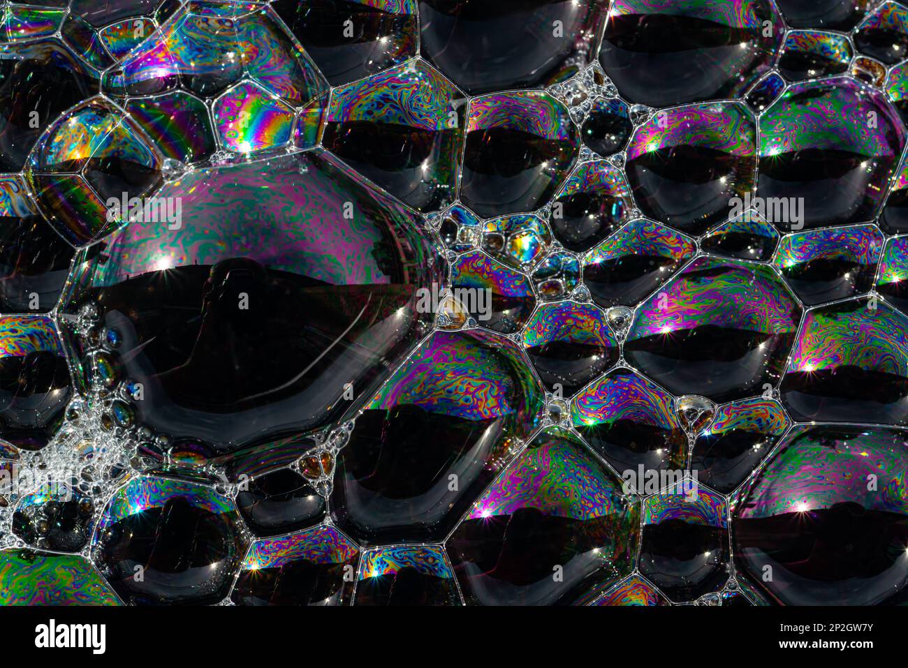 Gros plan, photo macro d'une bulle de savon, arc-en-ciel multicolore avec couleurs jaune, violet, rose, bleu et vert sur fond noir. Banque D'Images