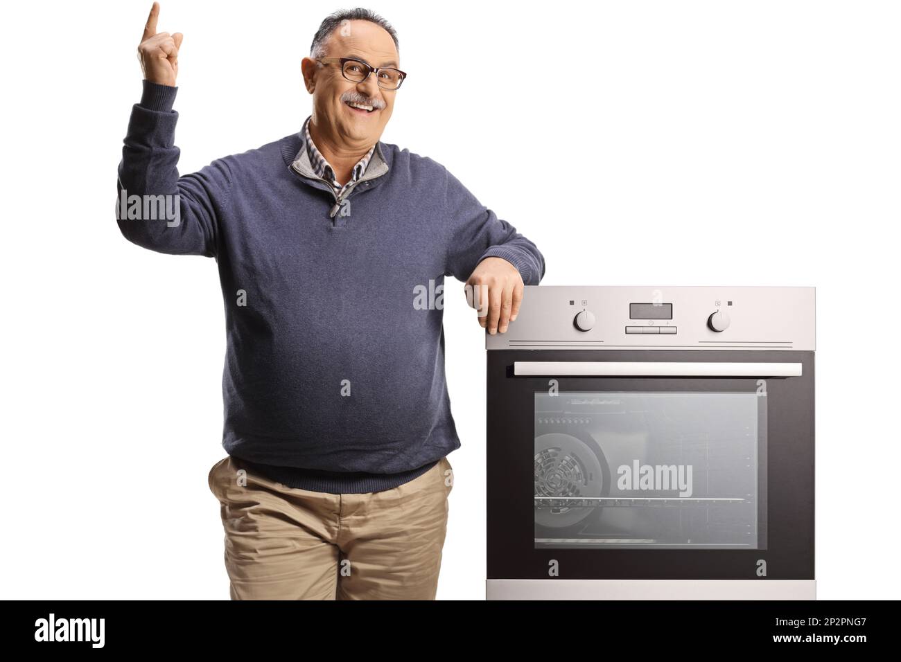 Homme mûr souriant penché sur un four et pointant vers le haut isolé sur fond blanc Banque D'Images