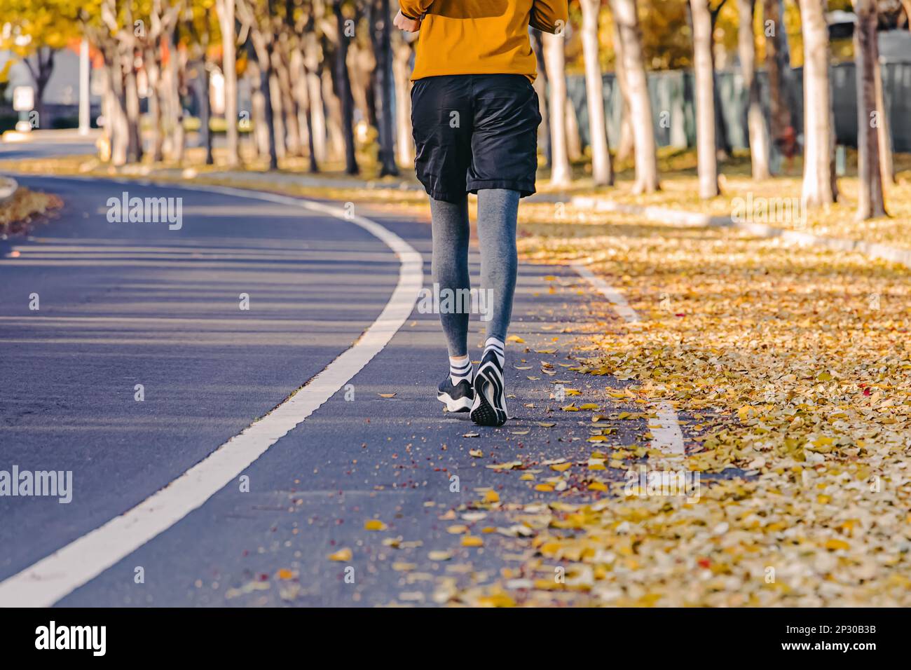 Vue depuis l'arrière de l'homme méconnu qui fait du jogging à l'extérieur à l'automne. Feuilles jaunes dans la rue, en automne Banque D'Images