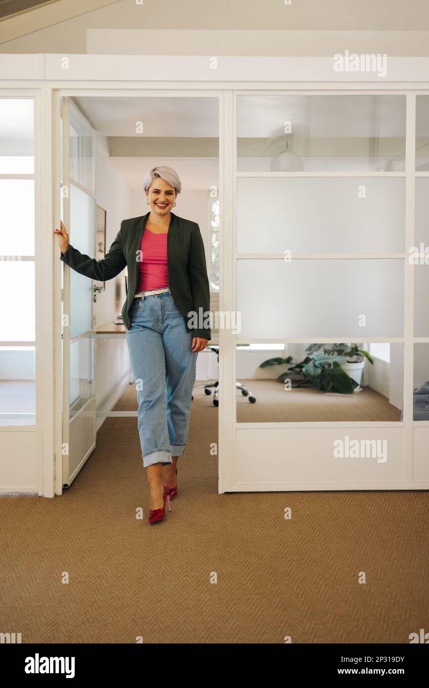 Femme d'affaires qui a réussi à sourire à la caméra tout en se tenant devant son bureau. Une femme entrepreneure heureuse travaillant dans un milieu de travail créatif. Banque D'Images