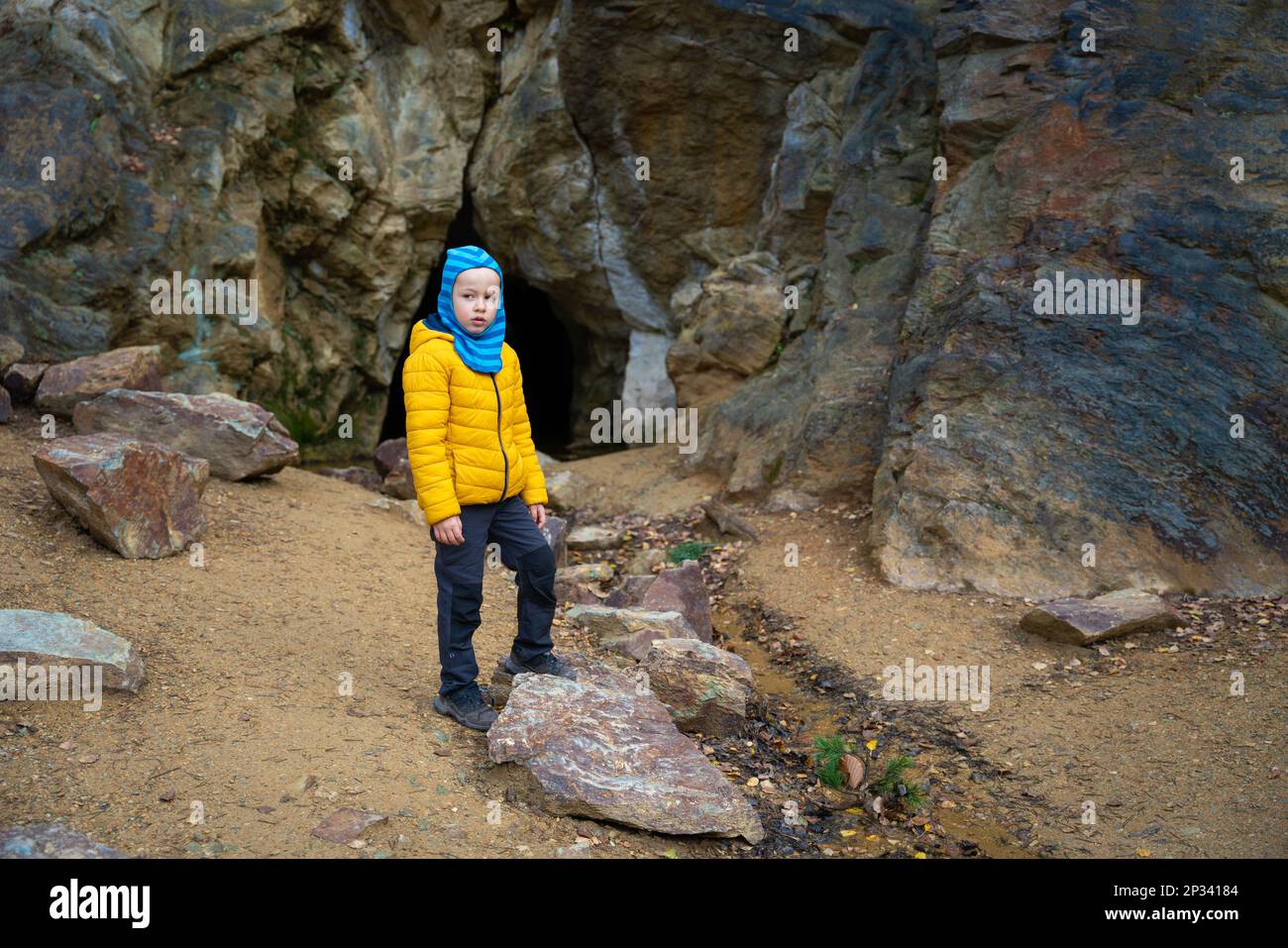 Un petit garçon se tient près des rochers en arrière-plan de l'entrée d'une petite grotte. Montagnes polonaises Banque D'Images