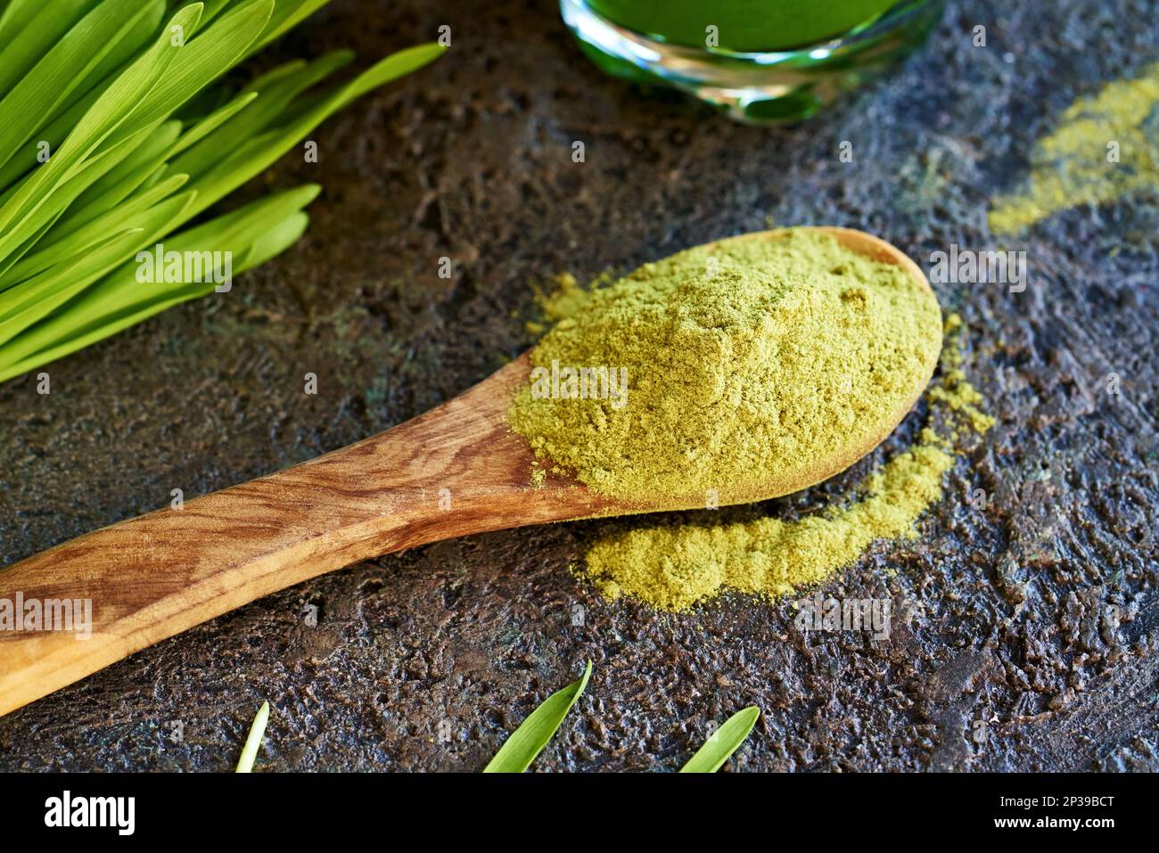 Poudre d'orge séchée sur une cuillère avec des lames fraîches et du jus vert en arrière-plan Banque D'Images