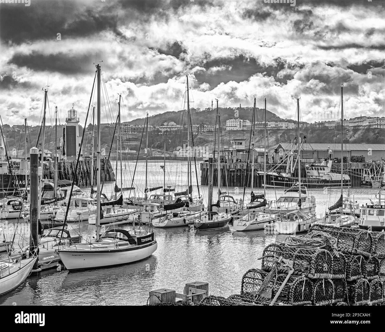 Une marina de yachts avec de hauts mâts. Les marmites de homard sont en premier plan et la colline avec des bâtiments est en arrière-plan. Un ciel nuageux est au-dessus. Banque D'Images