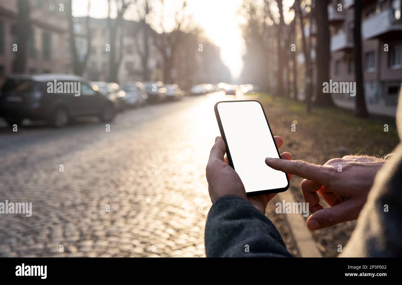 Homme touchant l'écran du téléphone portable avec le doigt sur l'arrière-plan de la route urbaine. Banque D'Images