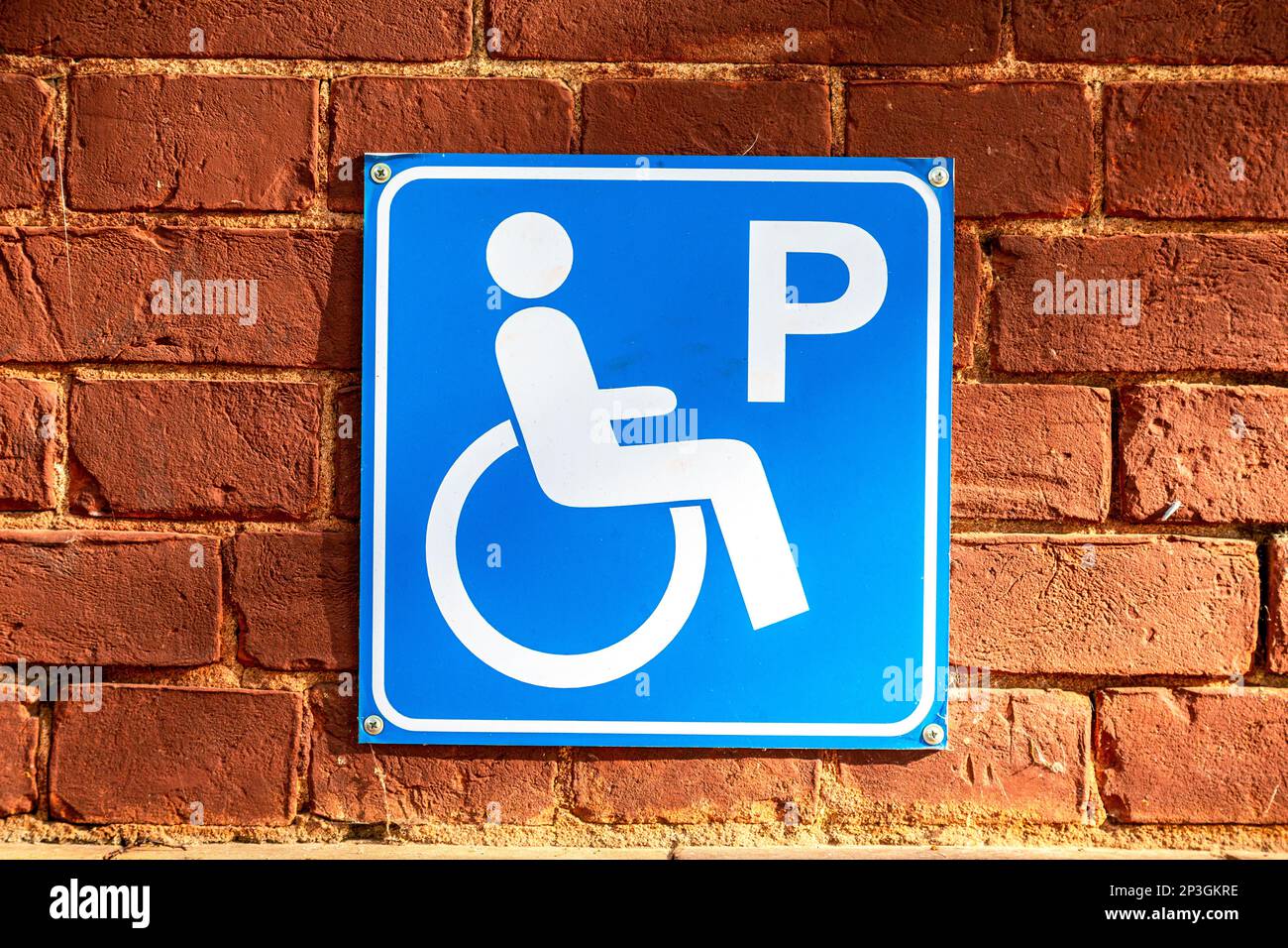 Icône de stationnement pour personnes handicapées sur le mur en brique rouge de près. Symbole fauteuil roulant Banque D'Images