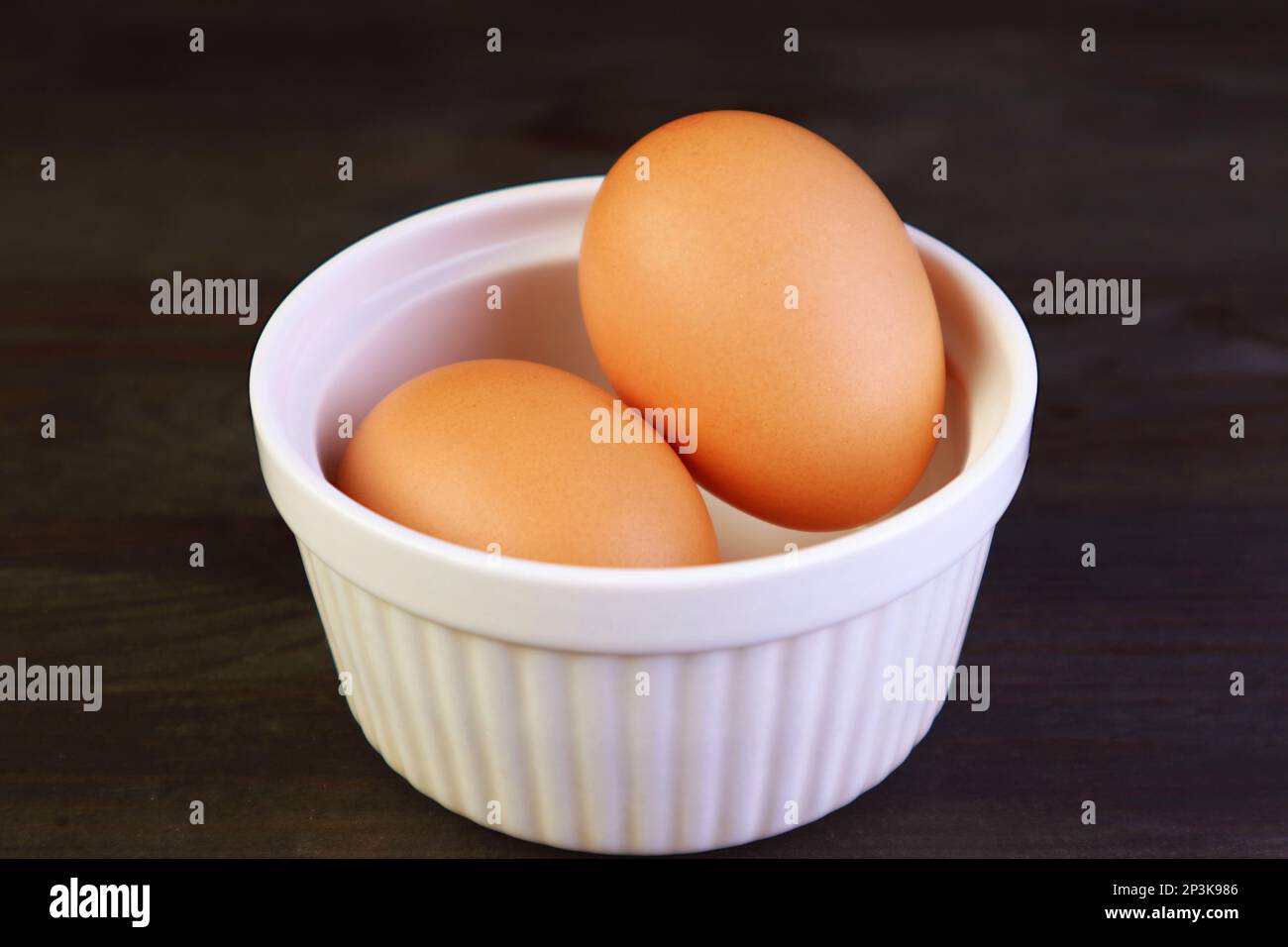 Gros plan des œufs de poulet dans un bol blanc isolé sur une table en bois noir Banque D'Images
