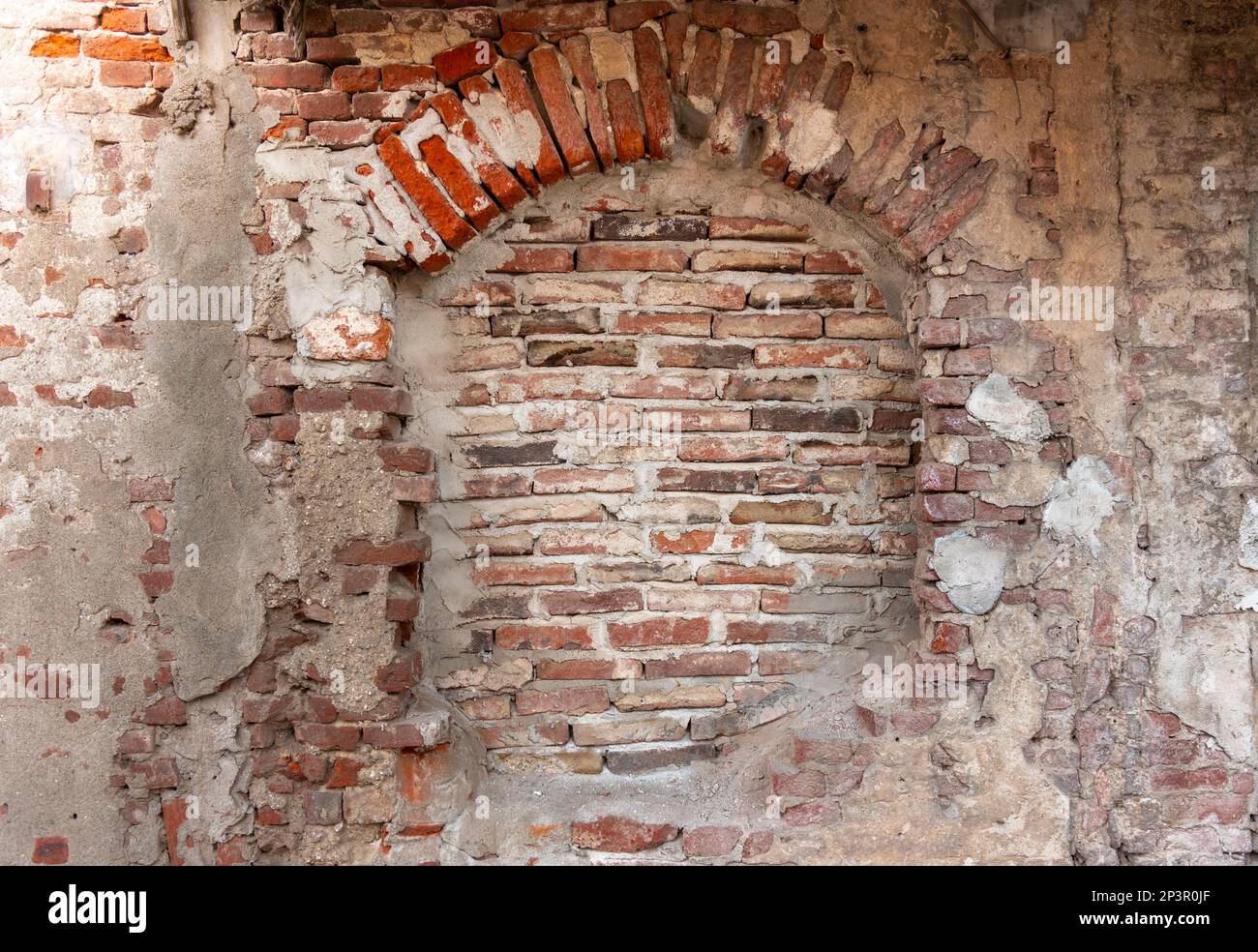 Texture murale avec plâtre ancien et arrière-plan peeling avec brique rouge exposée. Ancienne fenêtre voûtée en briques Banque D'Images