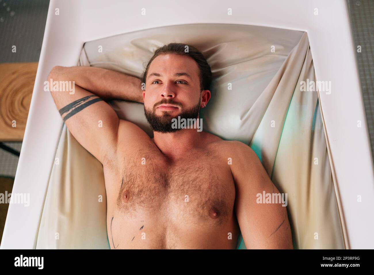 Portrait en haut de la vue d'un jeune homme beau à barbe allongé sur un lit de massage électrique et profitant d'un soin spa au luxueux spa salon. Banque D'Images
