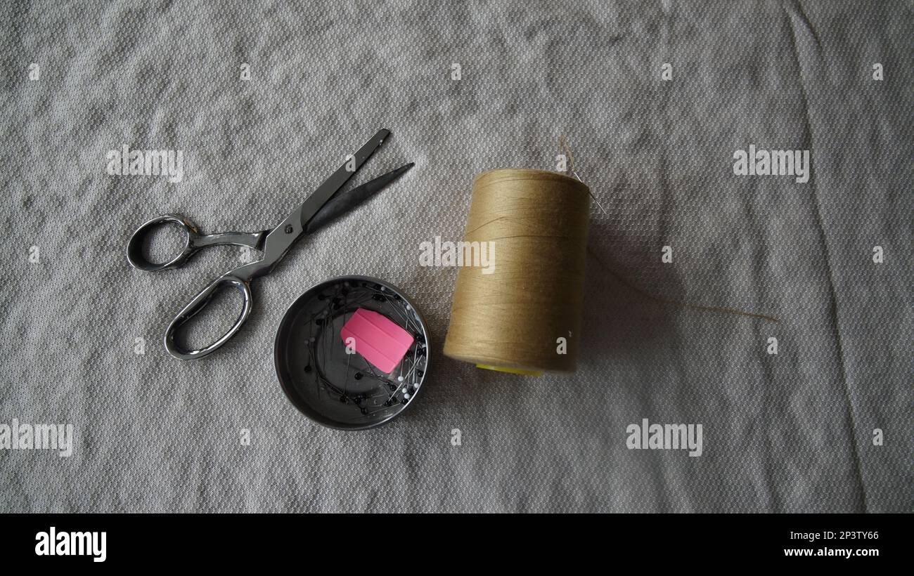 Vue de dessus des matériaux de couture. Ciseaux, fil et aiguille sur un fond de tissu. Banque D'Images