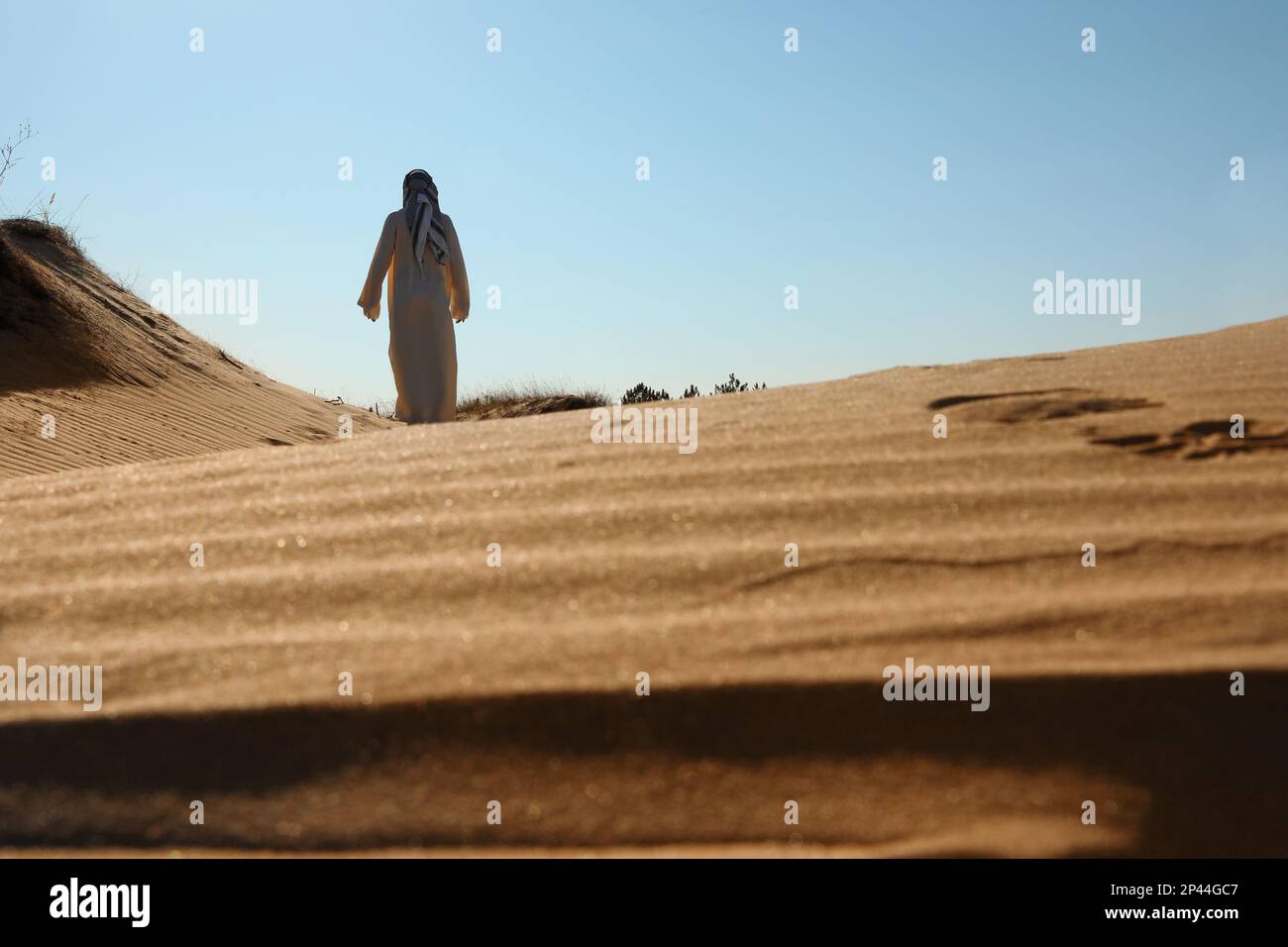 Homme en vêtements arabes marchant dans le désert le jour ensoleillé, vue arrière Banque D'Images