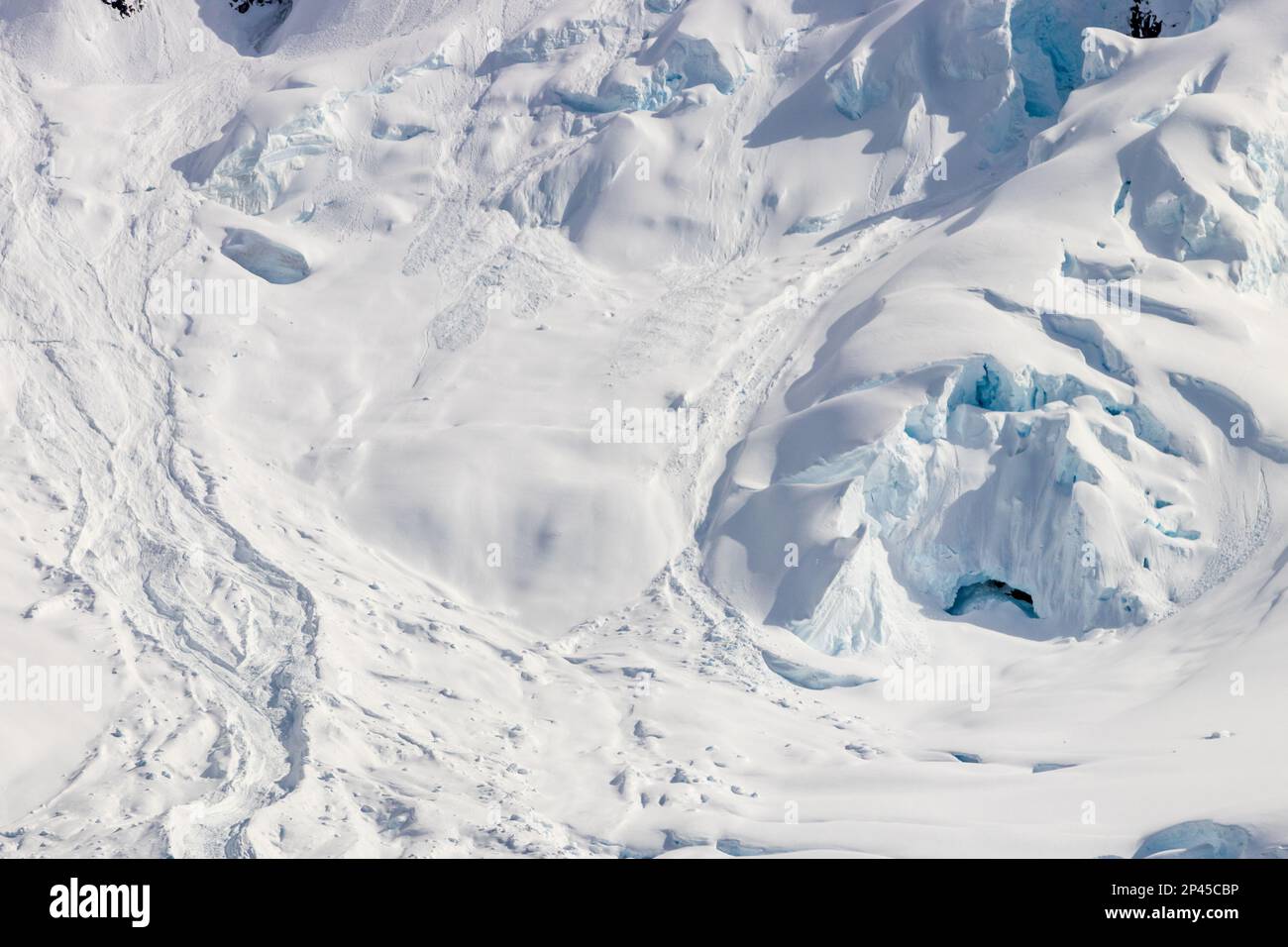 Pente de montagne enneigée, péninsule antarctique. Roches exposées sur une pente enneigée. Glace bleue visible ; ouverture à la grotte de glace. Banque D'Images